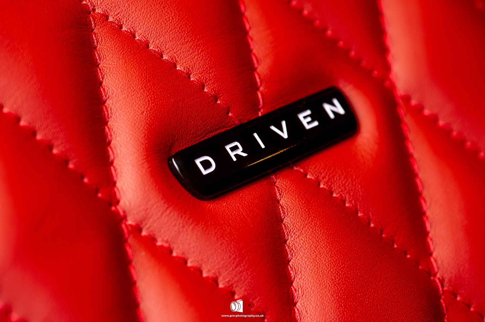 Close-up shot of red quilted leather car interior with a black "Driven" emblem for a stylish aesthetic.