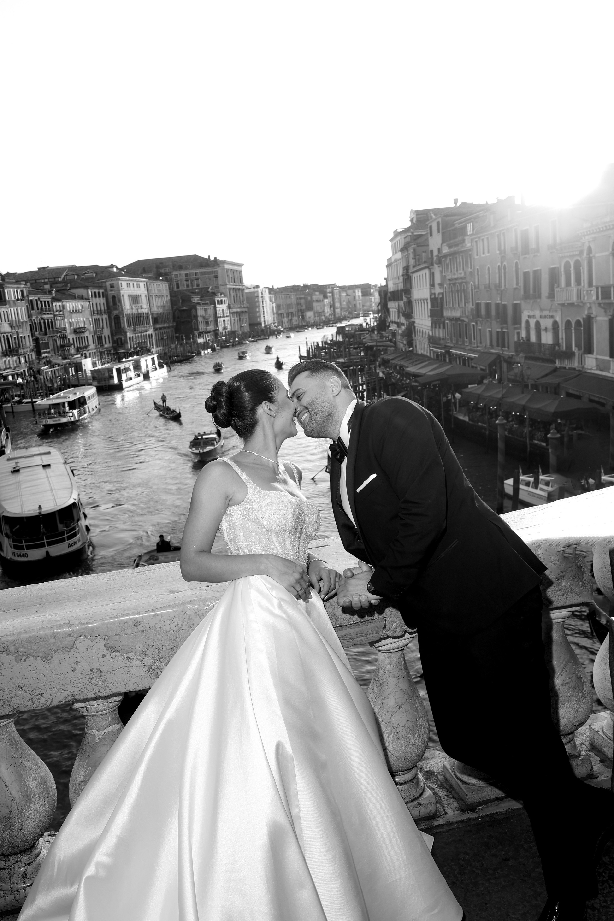 Bride and groom posing on a Venetian square with canals and a gondola in the background