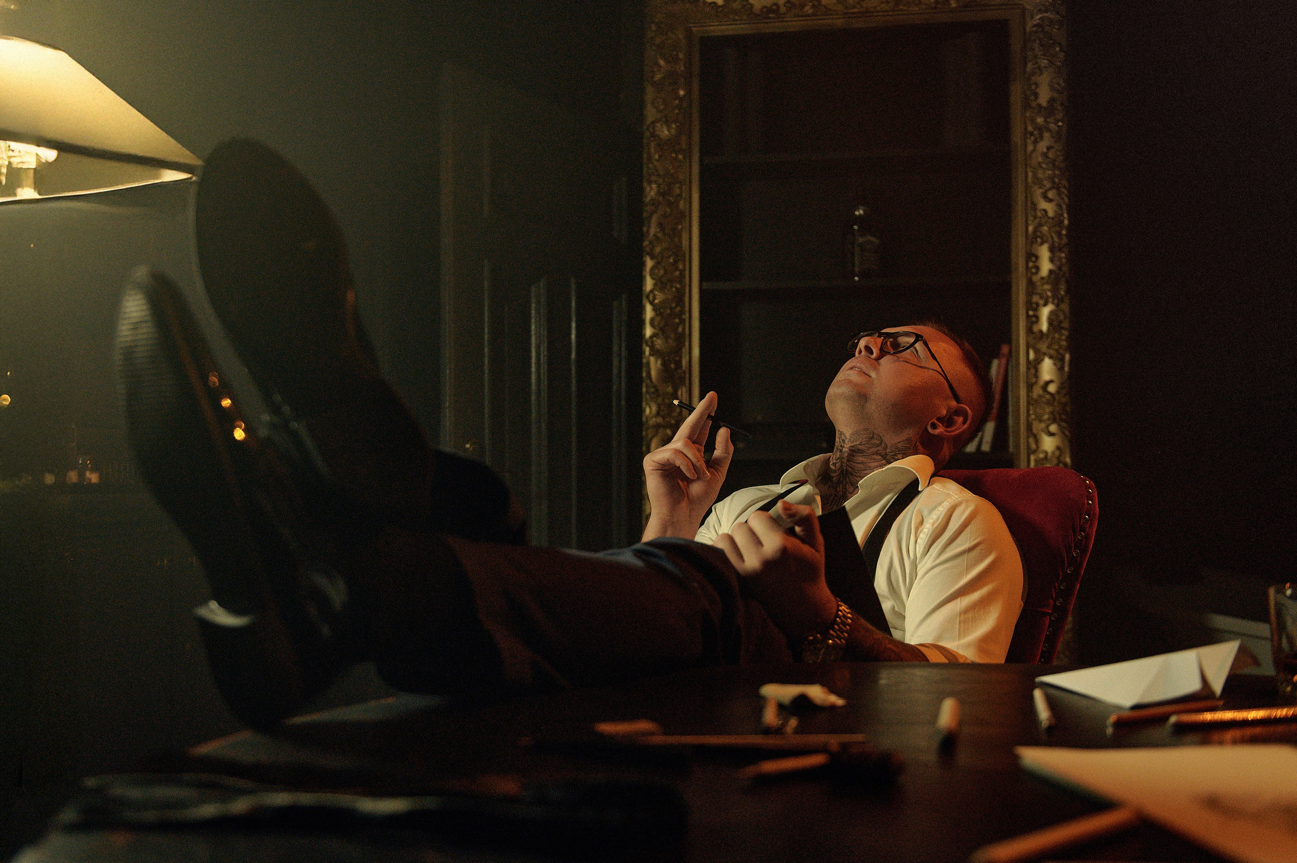 Artystyczne ujęcie – mężczyzna z tatuażami, z ołówkiem, siedzi z nogami na biurku, patrzy w sufit