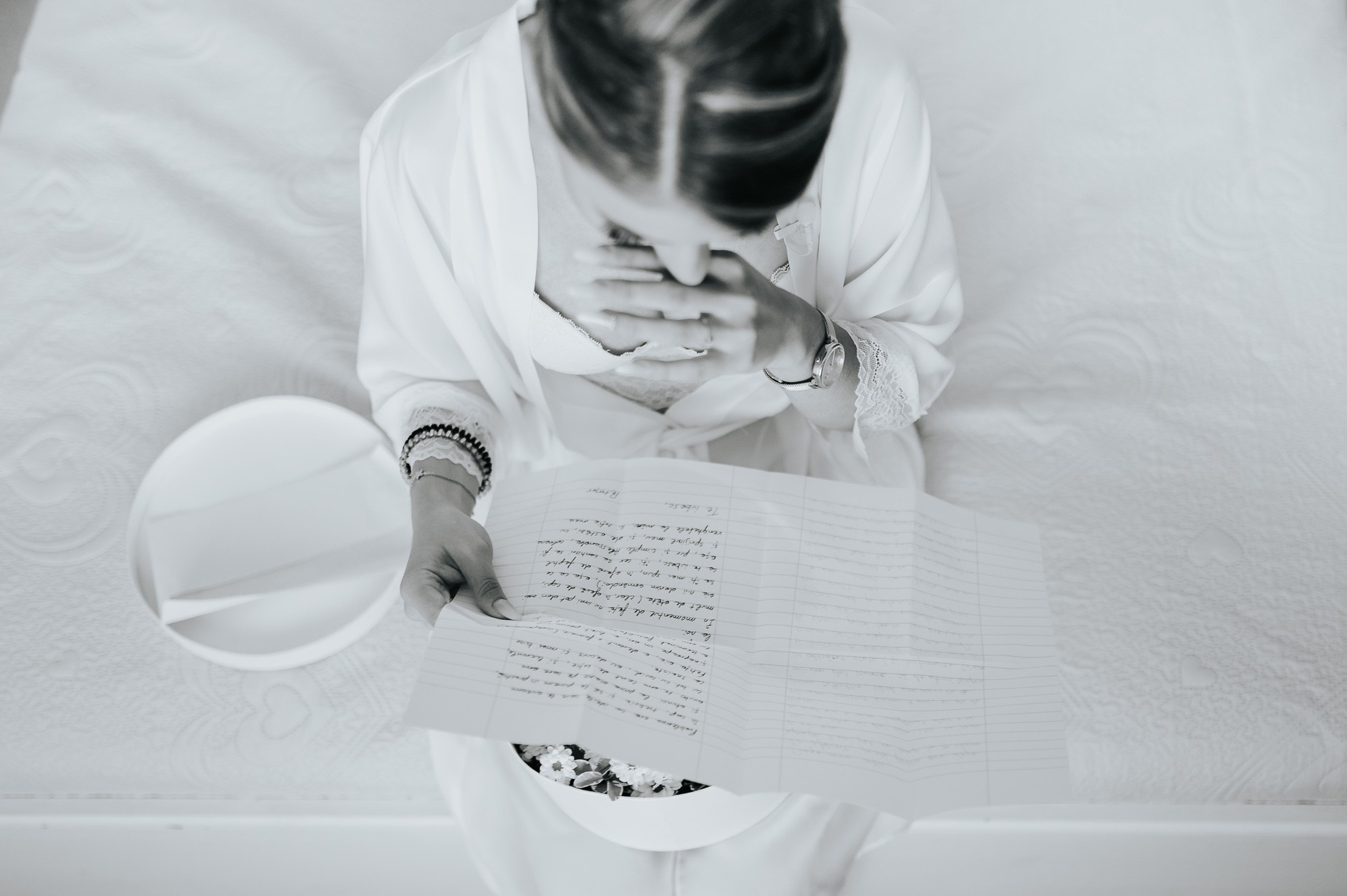 Vista dall'alto di una sposa commossa che legge una lettera d'amore, con una mano sul viso, seduta in un ambiente elegante, con un'atmosfera intima e sentimentale prima del matrimonio.