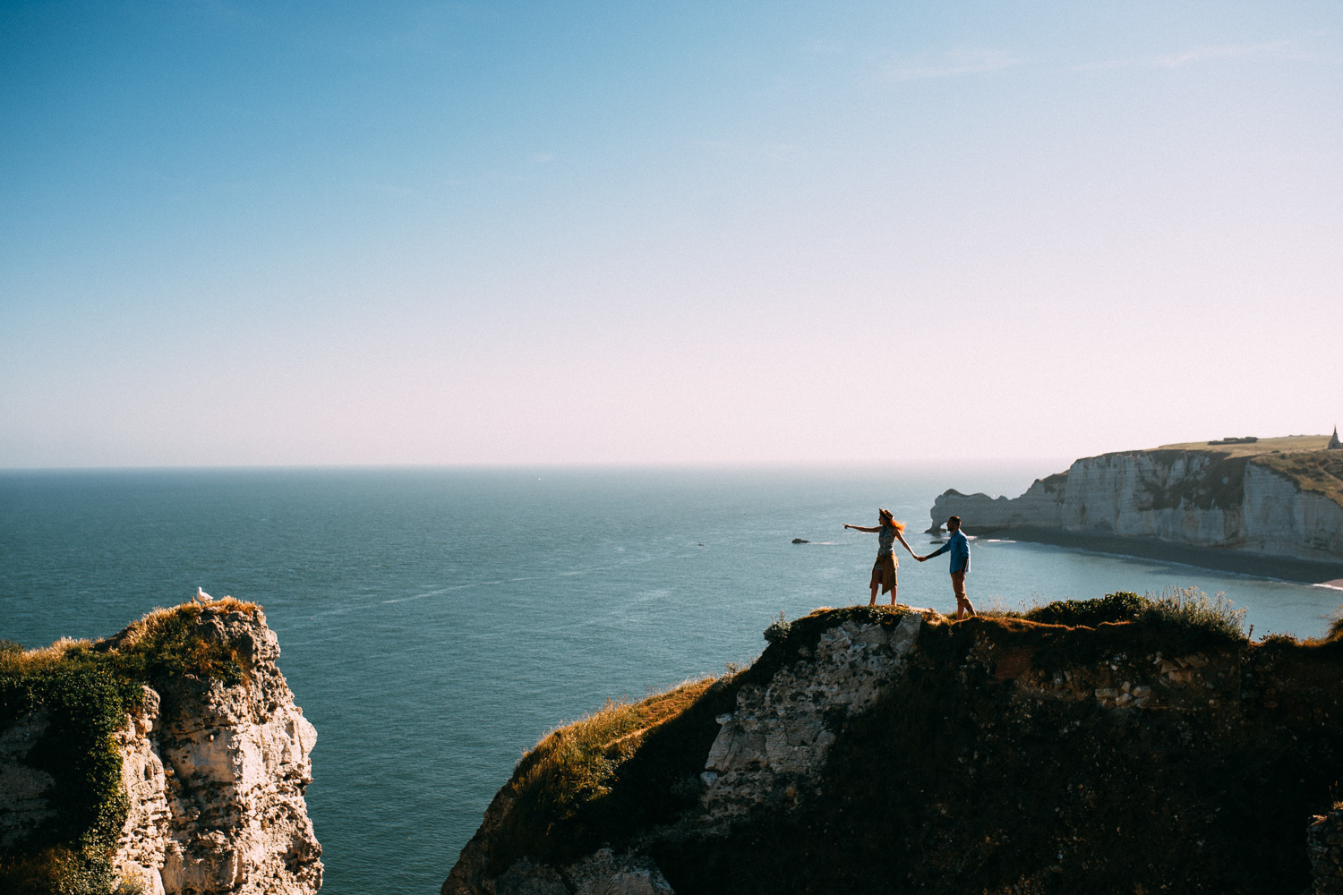 Newlyweds standing in front of the ocean on a high shore in Normandy.
