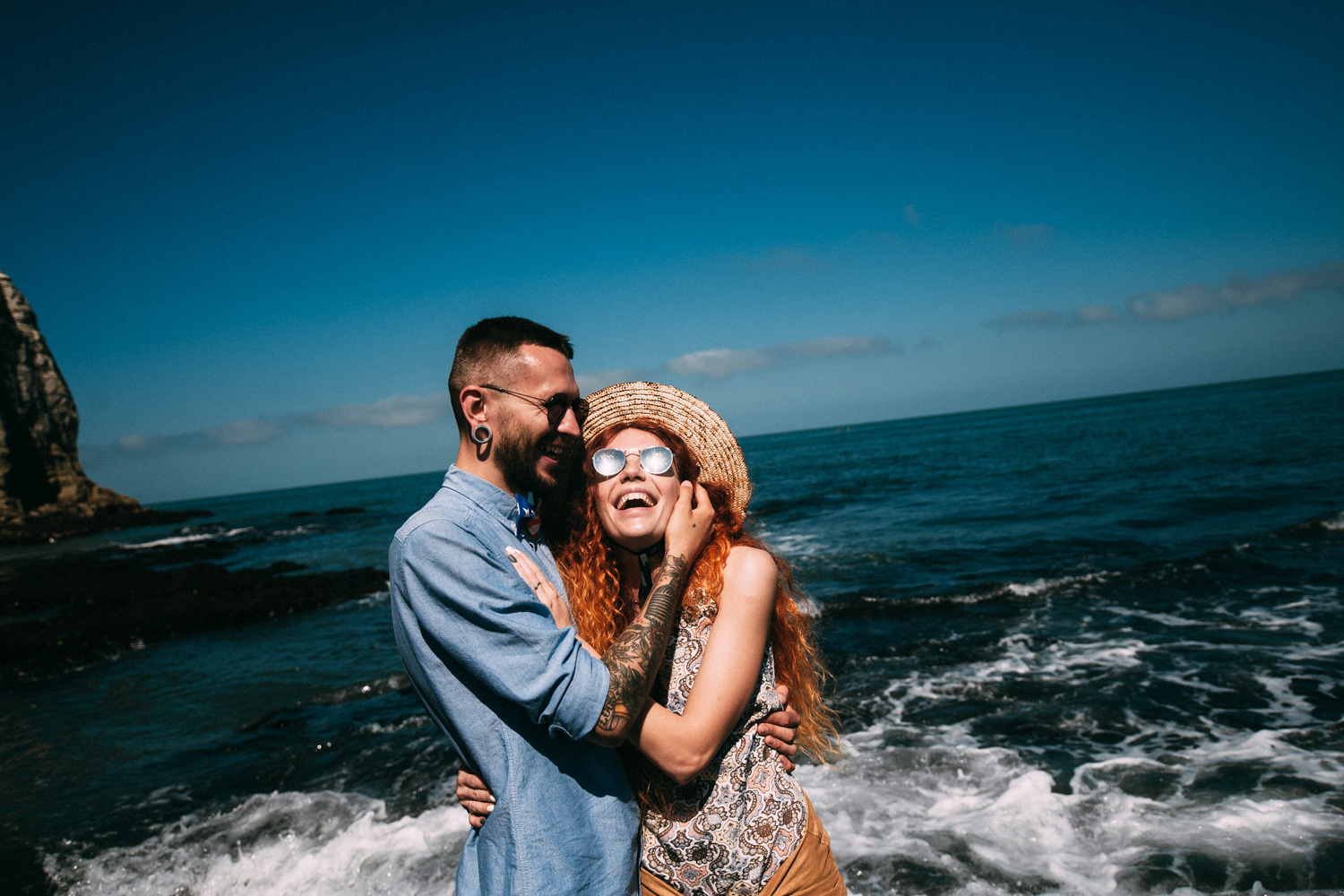 The newlyweds are smiling for the photographer, the bride has glasses and a hat.