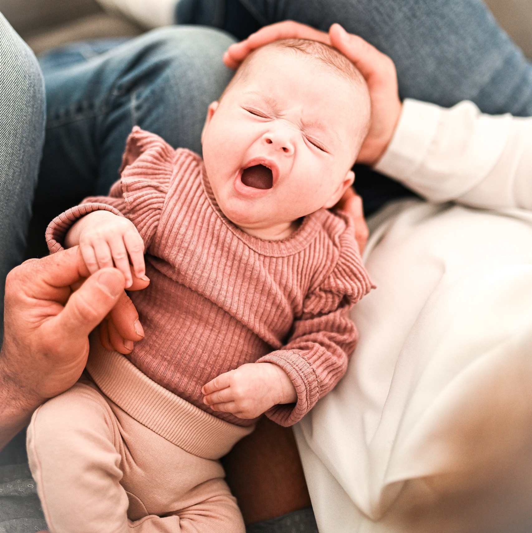 Das Baby gähnt, während es auf den Knien seiner Eltern liegt