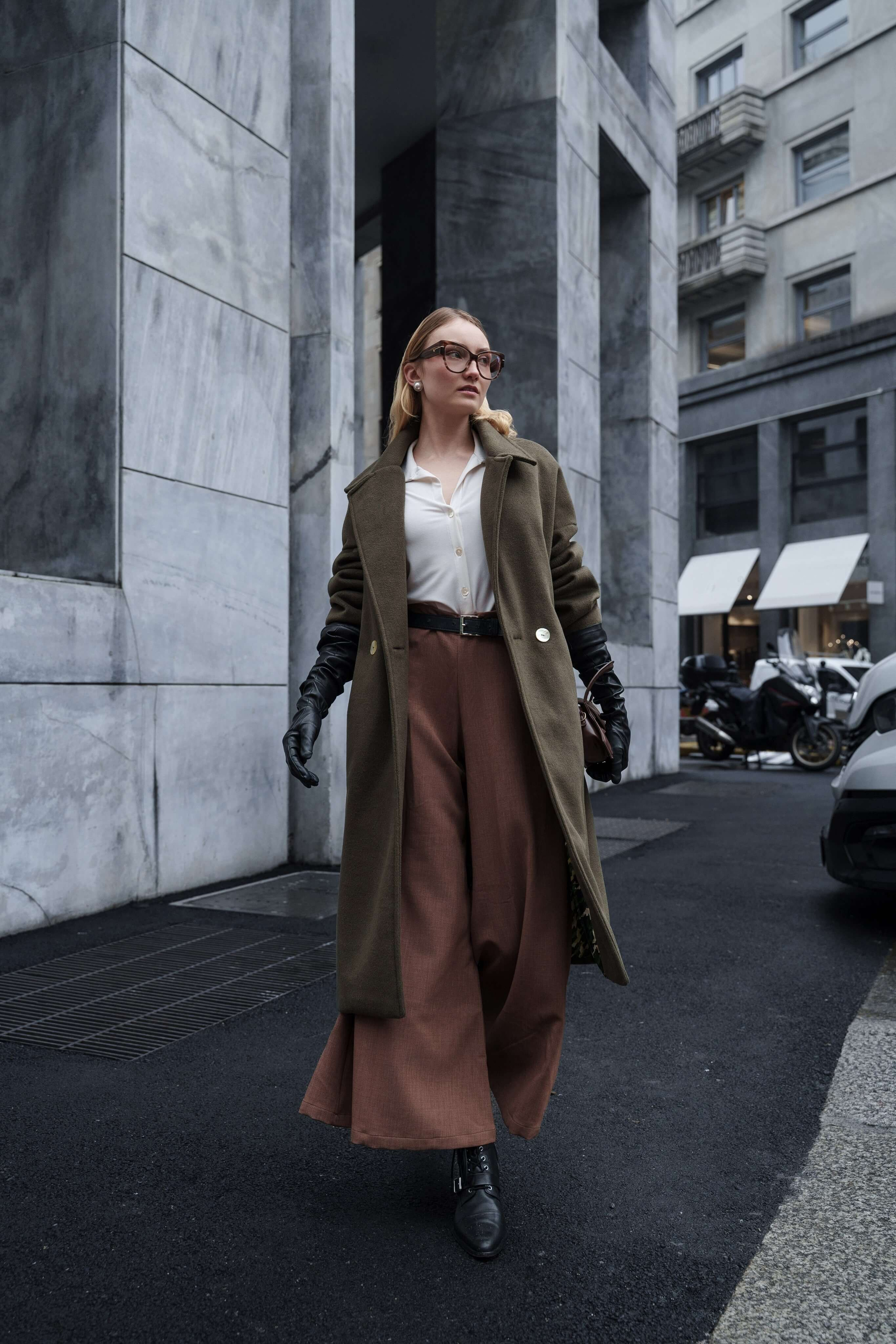 Fashion photographer captures female model walking confidently in wide pants and oversized coat during eyewear campaign