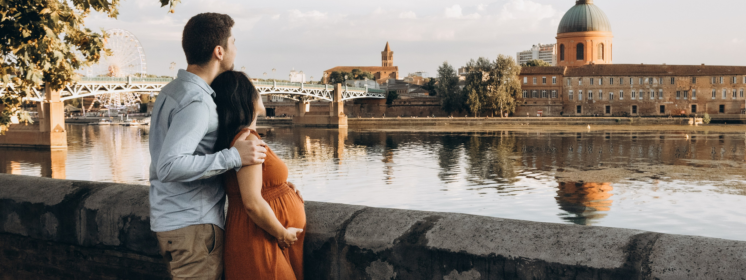 Couple of future parents watching the sunset on the board of the river Garonne in Toulouse