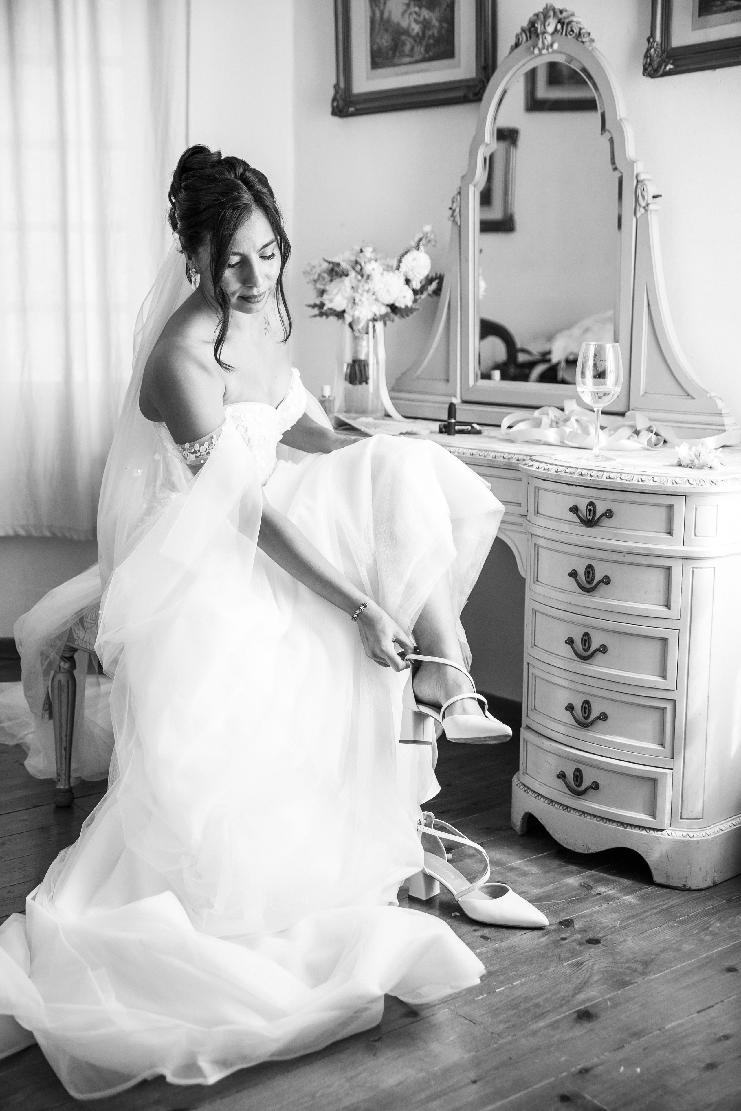 Black and white photo of a bride adjusting the shoes before walking down the aisle 