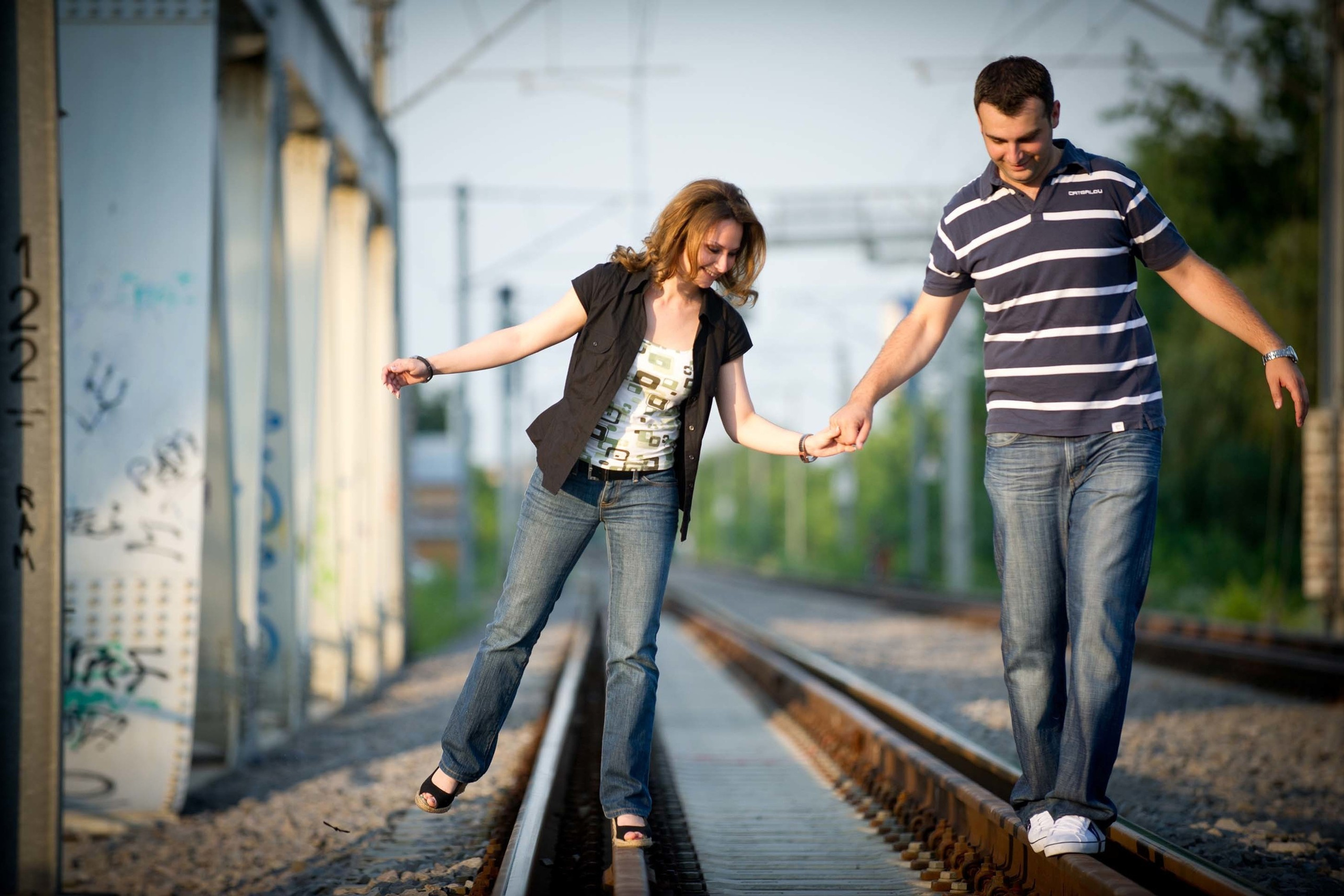 A couple holding hands and balancing on railway tracks during a fun and adventurous engagement shoot