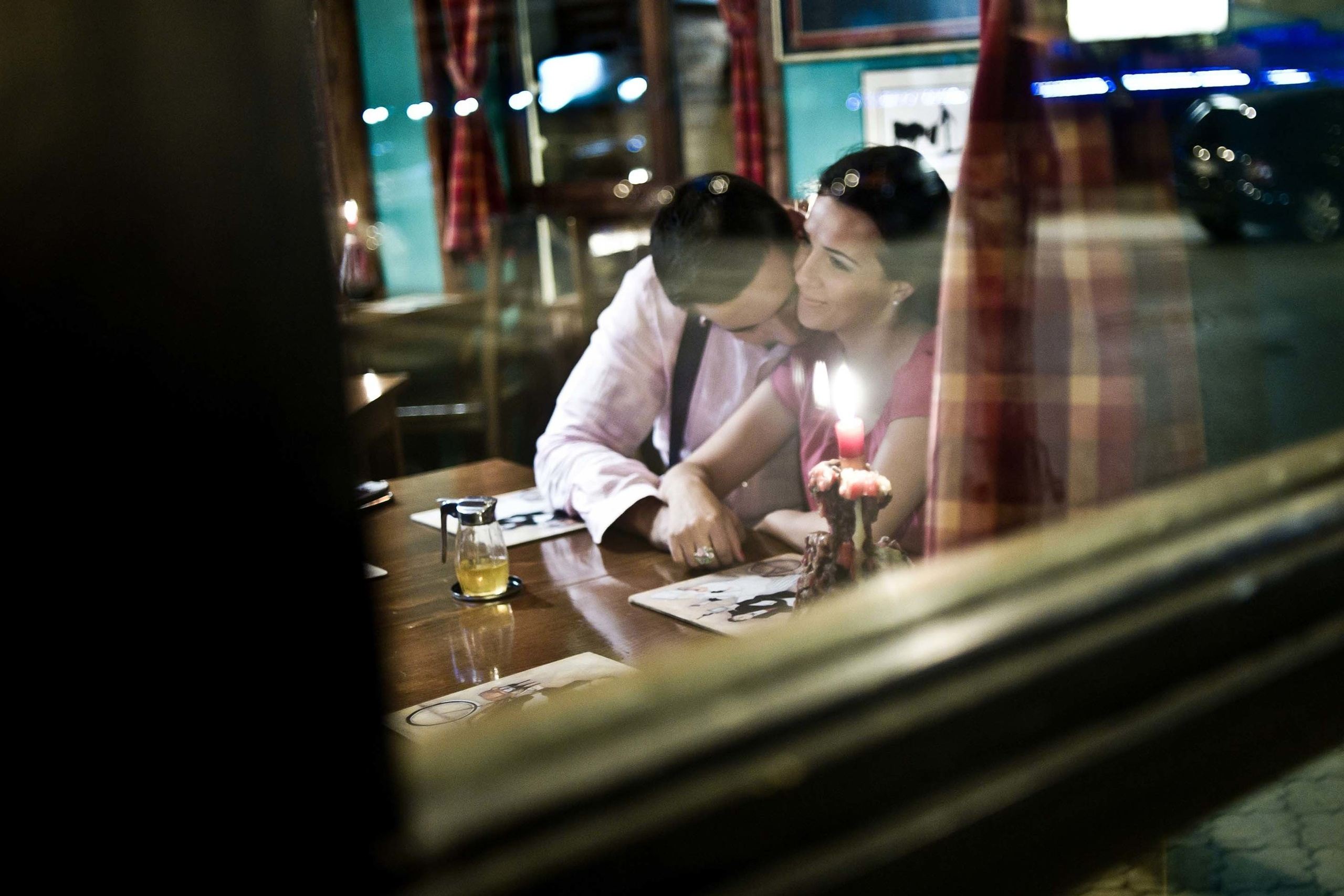  A couple sharing a romantic candlelit moment inside a cozy restaurant captured from outside through the window