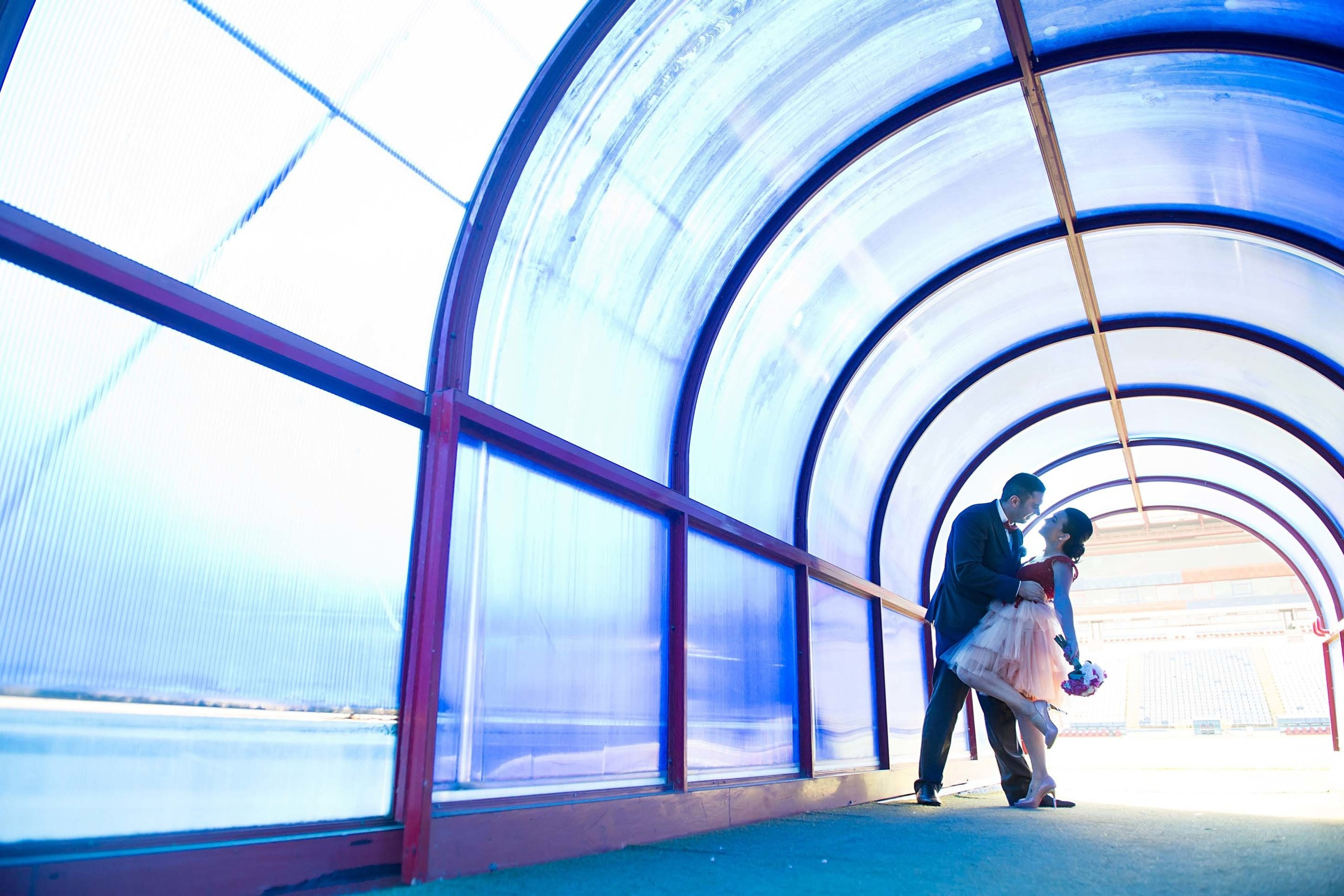 A couple is sharing a kiss in a blue-arched tunnel with romantic lighting
