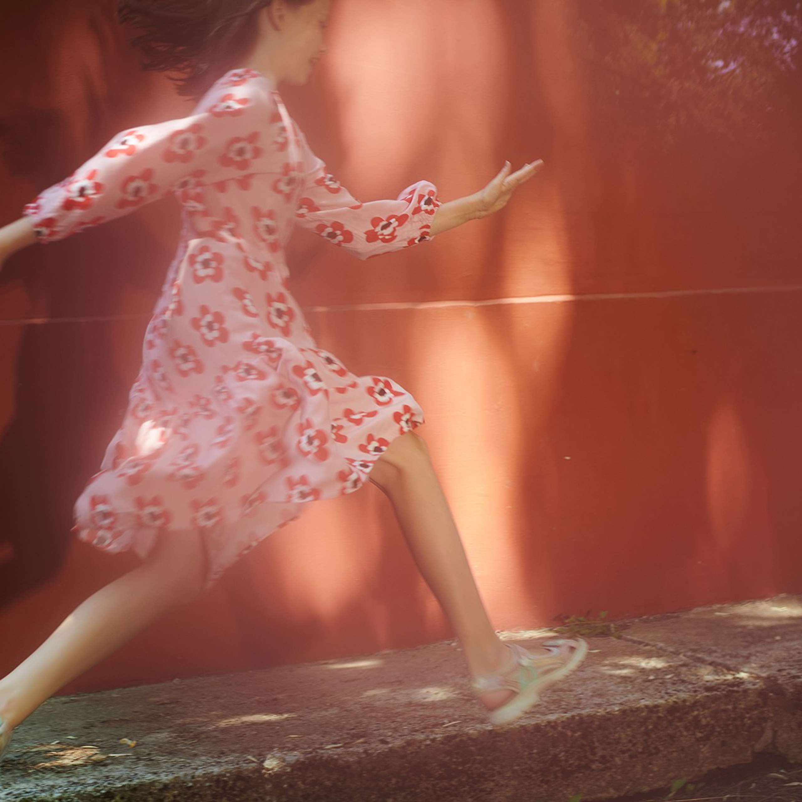 Artistic outdoor photoshoot of running girl in a pink dress in glare of light