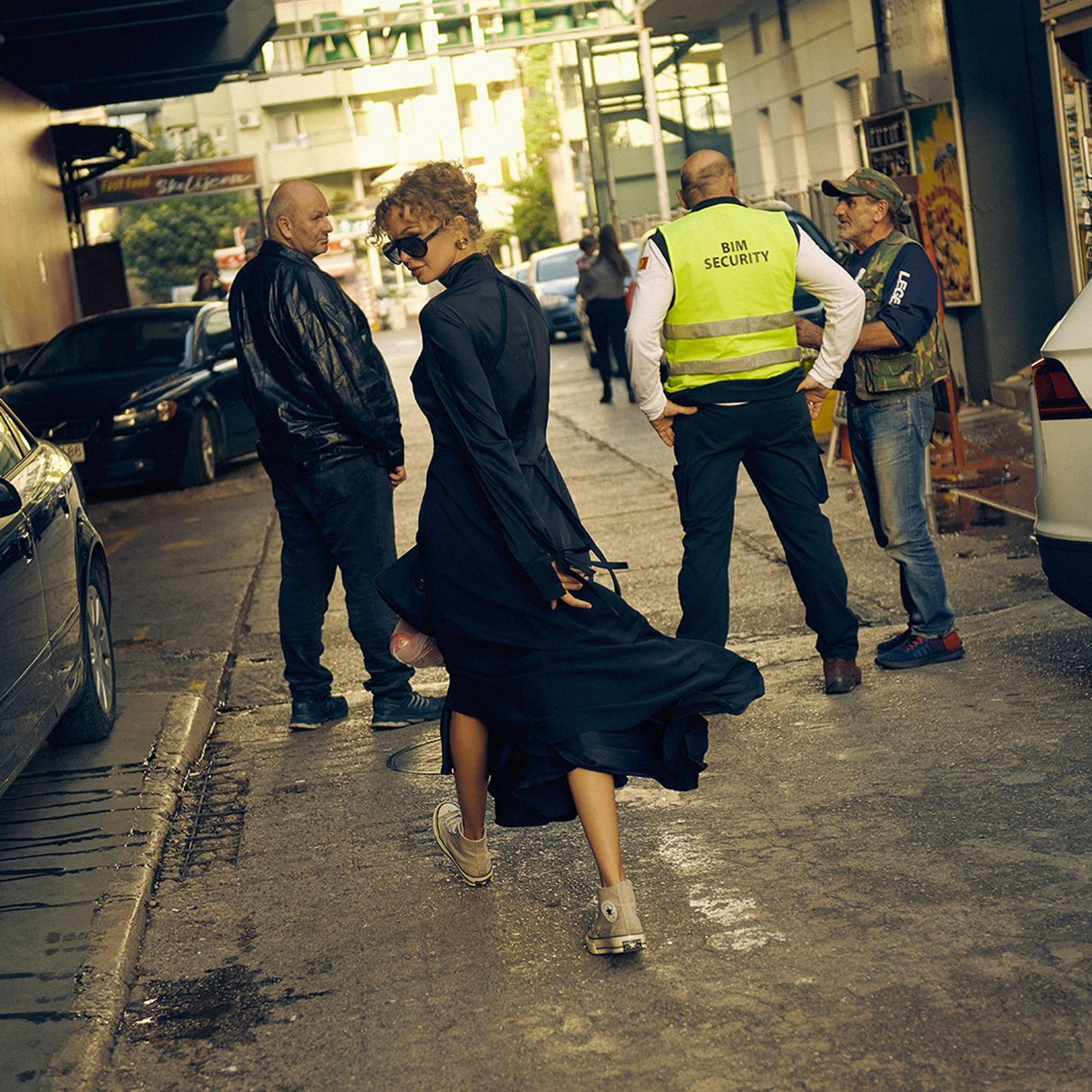 Fashion portrait of a woman with a curly hair wearing elegant black dressin a urban landscape, captured in natural light