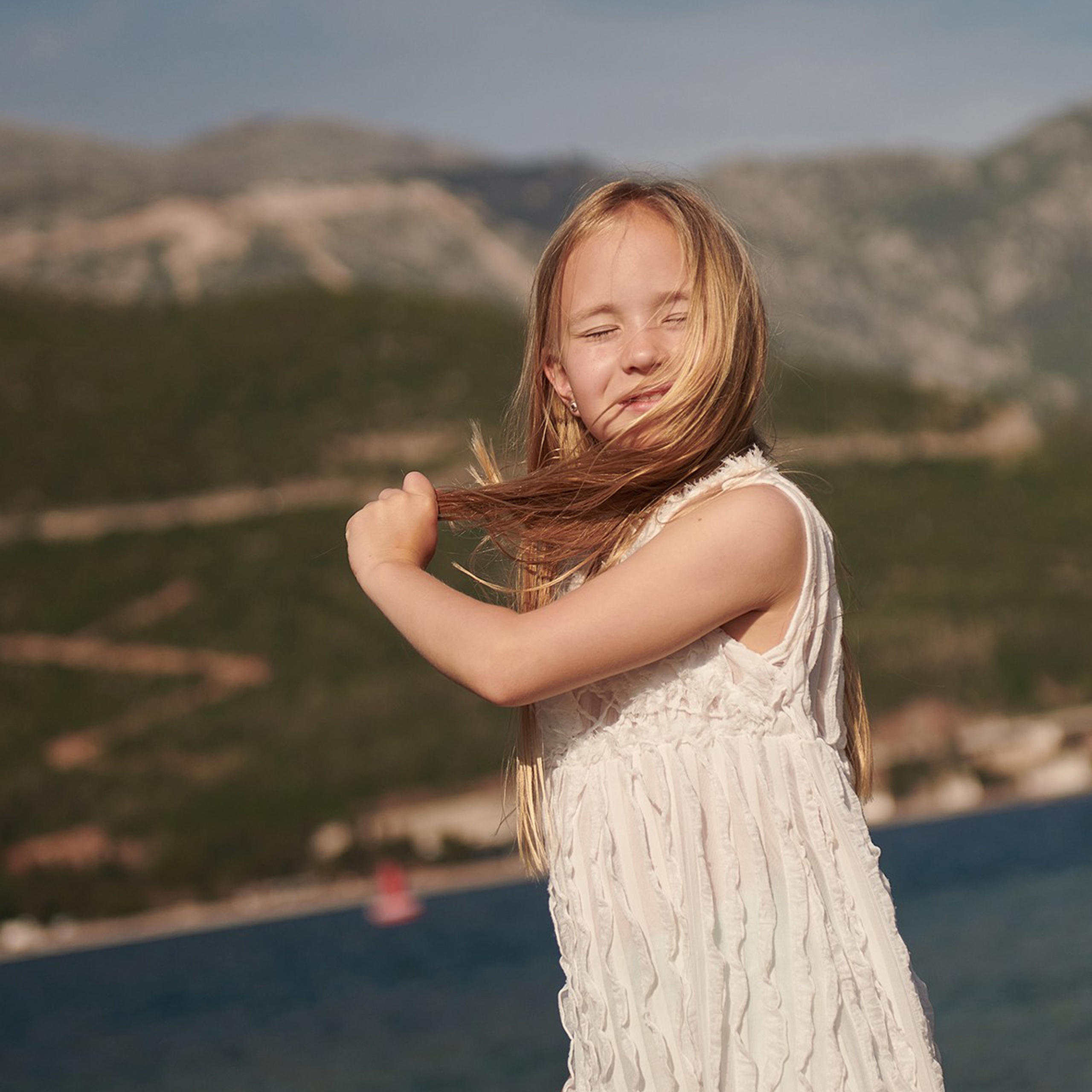 Lifestyle image for a kid's brand featuring a young girl in a white dress by the sea
