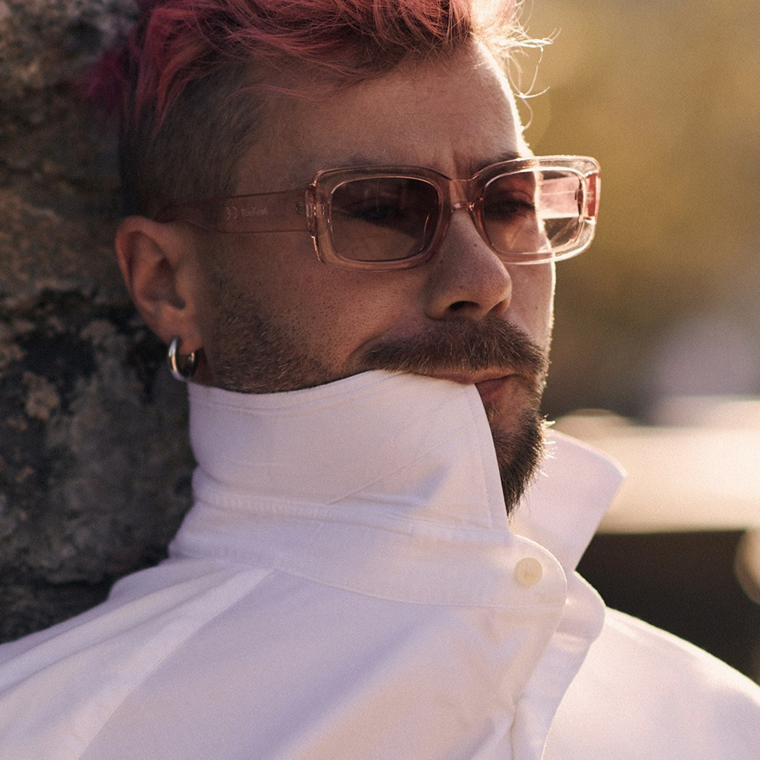 Portrait of a pink haired man in a white skirt showcasing stylish jewelry in a soft natural light 