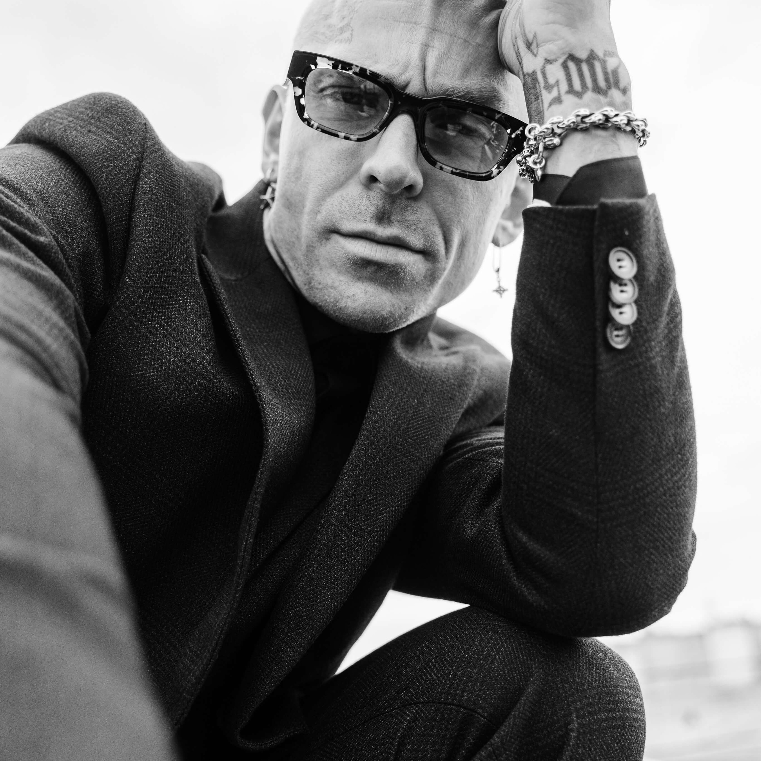 A monochromatic image showcasing a contemplative man in glasses, his detailed tattoos and thoughtful expression framed in the photographer's lens
