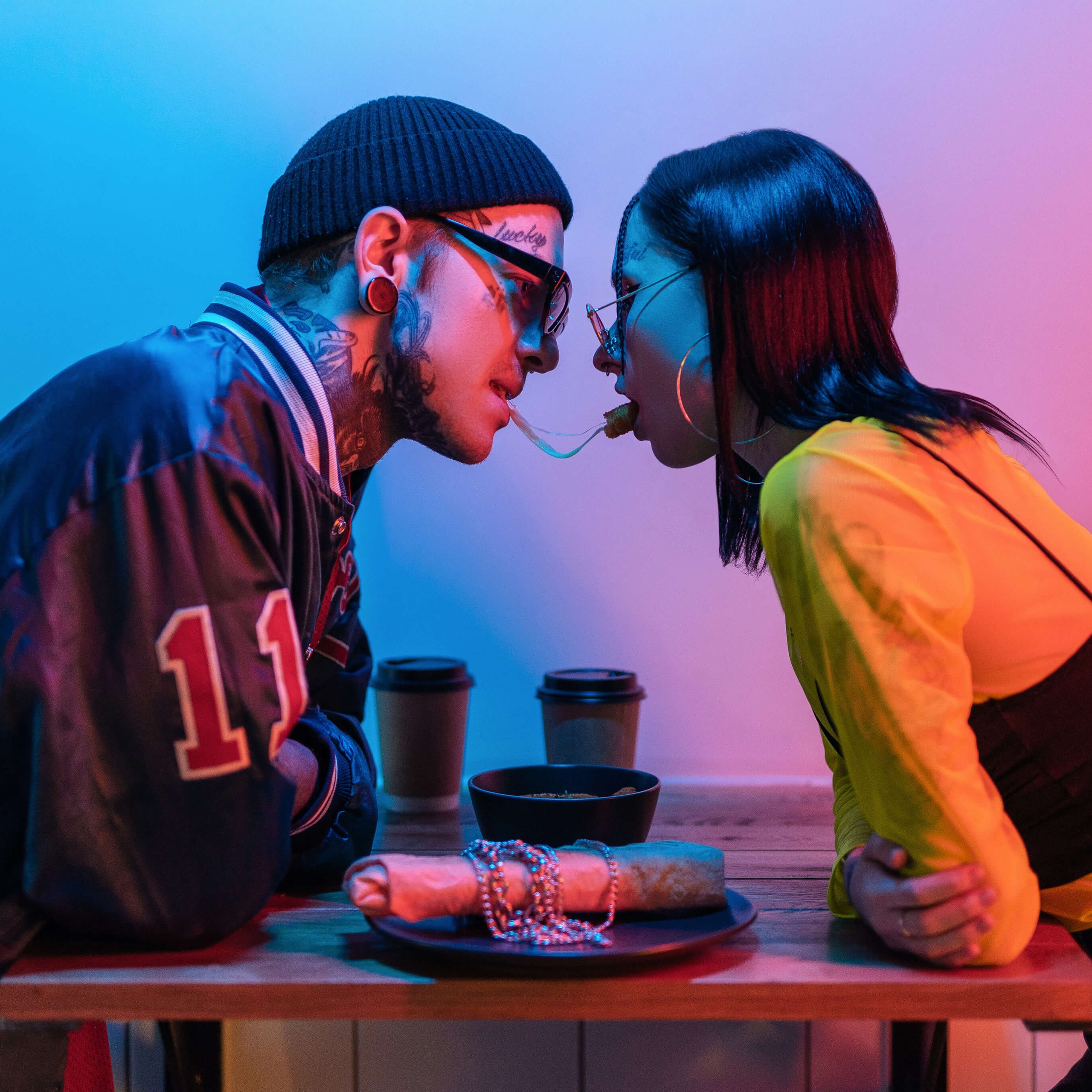 Two people sharing a spaghetti strand in a romantic gesture, illuminated by vibrant neon lighting that creates a contemporary and intimate atmosphere