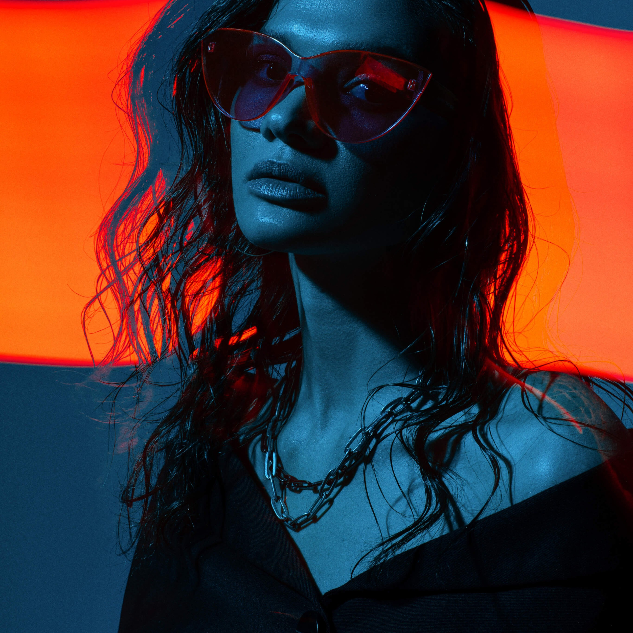 A dynamic portrait of a woman in sunglasses, her visage artfully illuminated by contrasting neon blue light with a bold red streak overhead, creating a vivid and stylish atmosphere