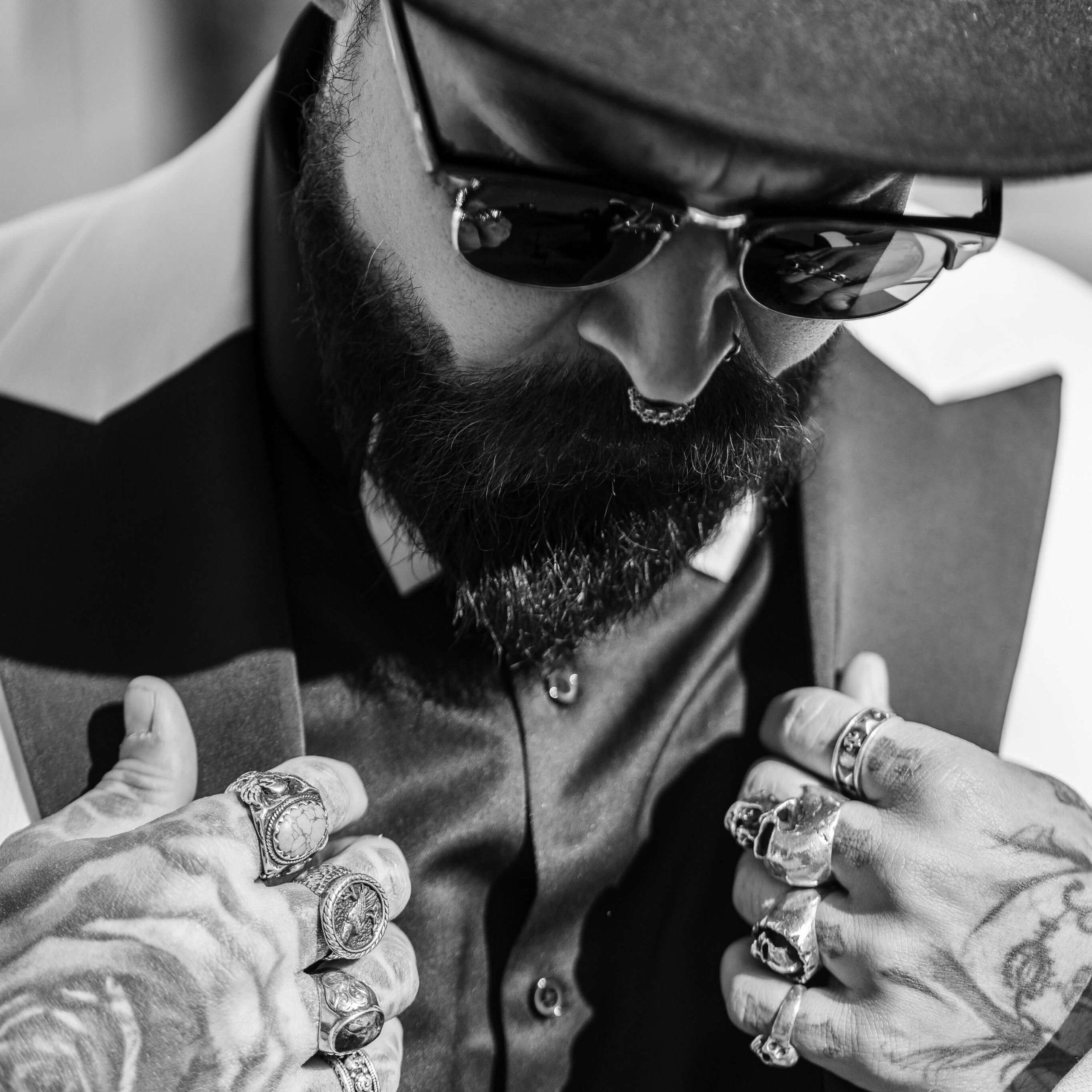 Black and white photo by a photographer of a bearded man in a fedora, focusing on his hands adorned with statement rings, showcasing detailed textures and personal style