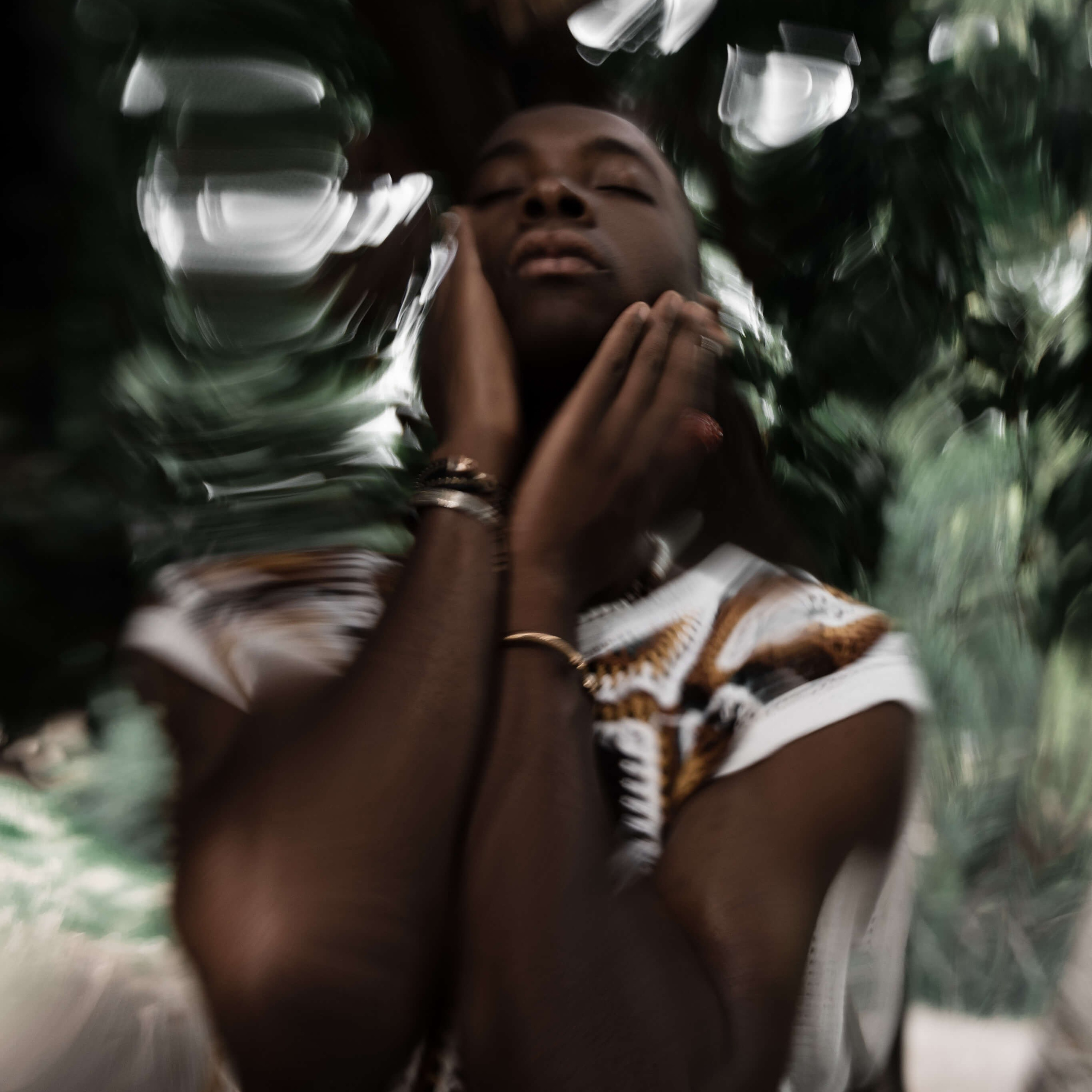 An artistic and abstract image by a photographer in Milan, portraying a contemplative moment with hands gently touching the face against a backdrop of blurred foliage
