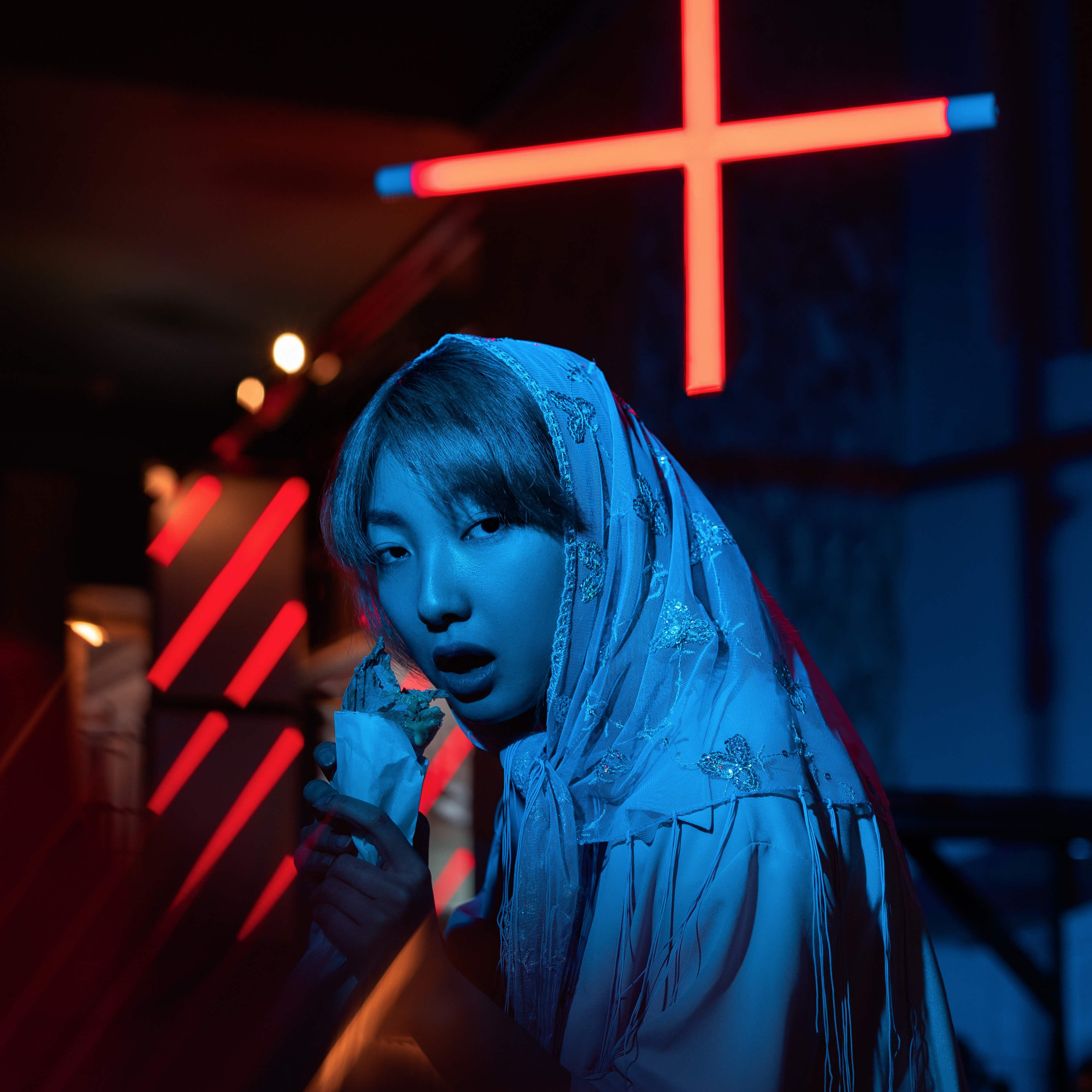 A captivating portrait of a person in a headscarf, illuminated by the ethereal glow of neon lights with a red cross in the background, creating a striking contrast and suggesting a narrative of intrigue