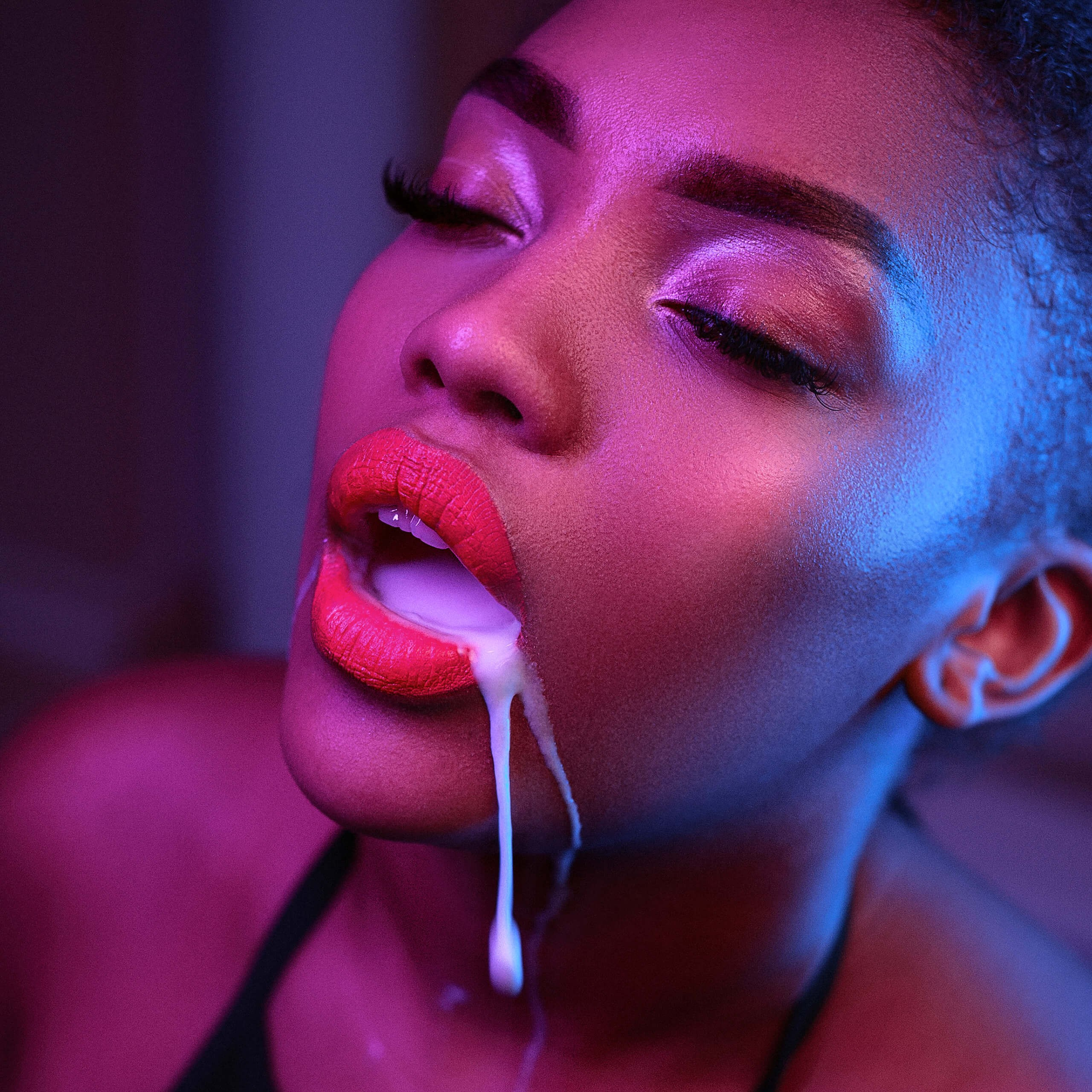 Artistic makeup photography by a Milanese artist, showcasing a woman's face with luscious red lips partly open, highlighted by neon lighting