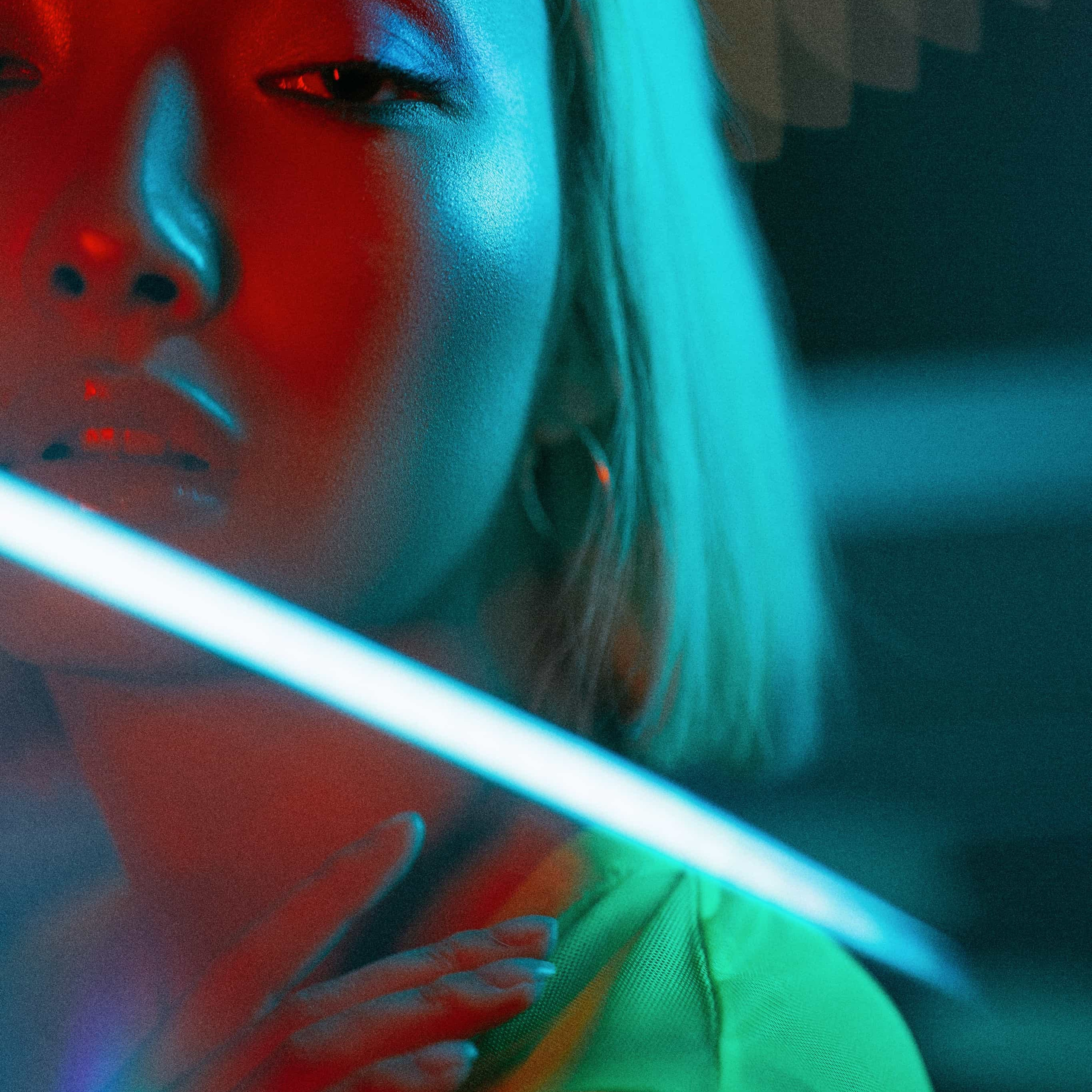 A close-up of a person bathed in neon blue and red lights, with a mysterious aura, accentuated by the shadows and the contemplative gaze