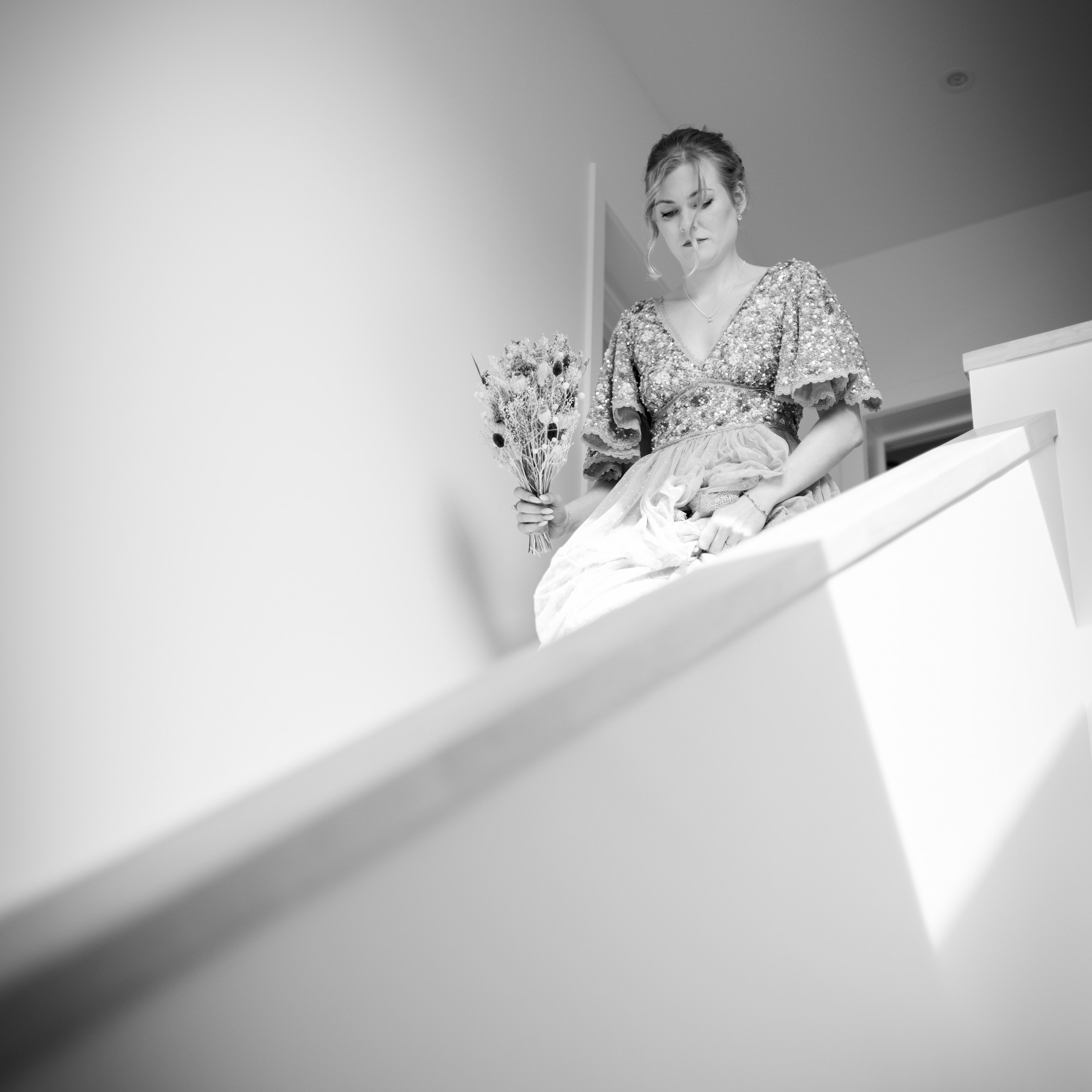Zwart-wit foto van bruid die de trap afkomt tijdens huwelijksvoorbereiding - Kapture Fotografie