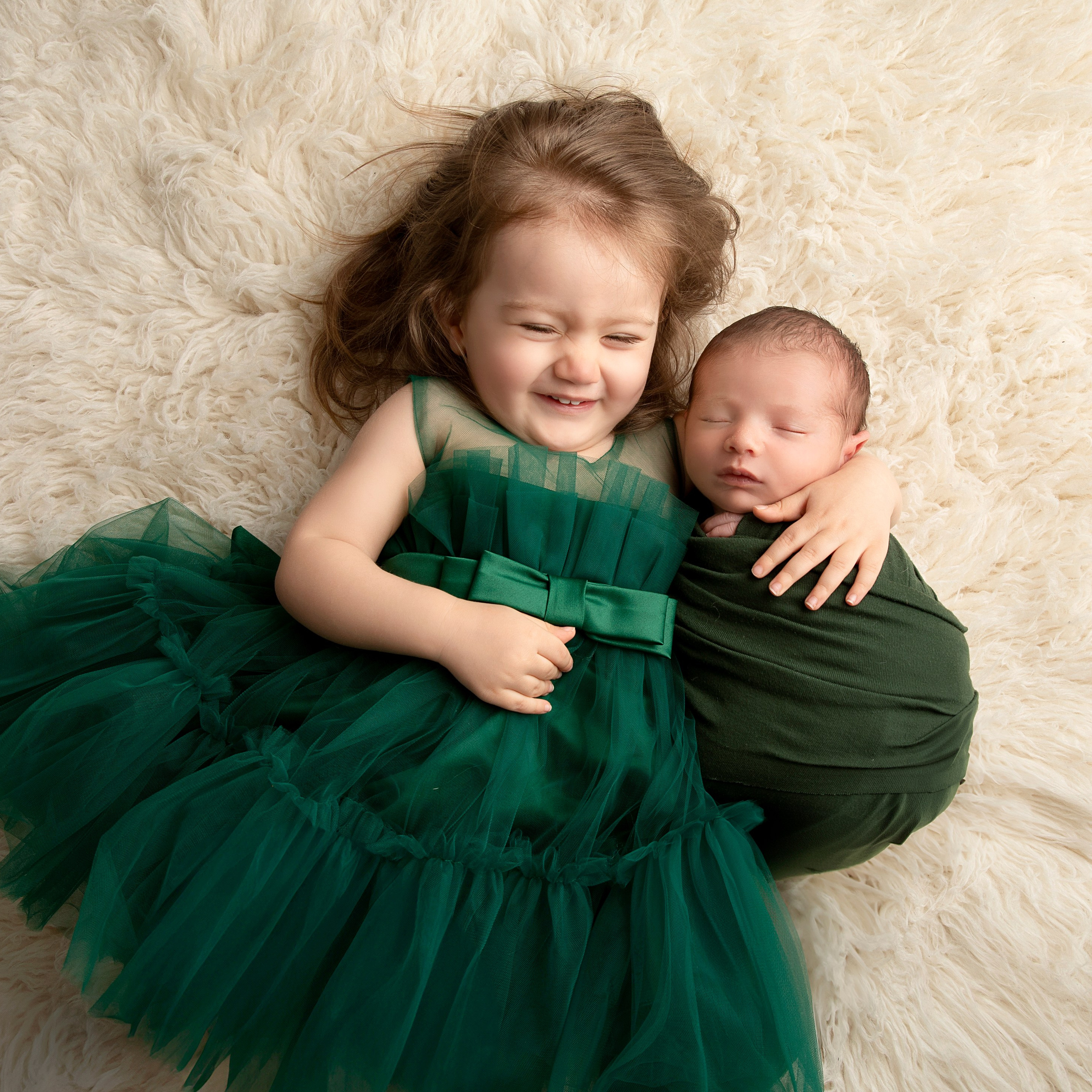 "Nyfödd bebis som ligger i knäet på sitt äldre syskon. Bilden visar den speciella relationen och ömheten mellan dem och passar utmärkt för att framhäva familjeband i nyfödda fotograferingar."