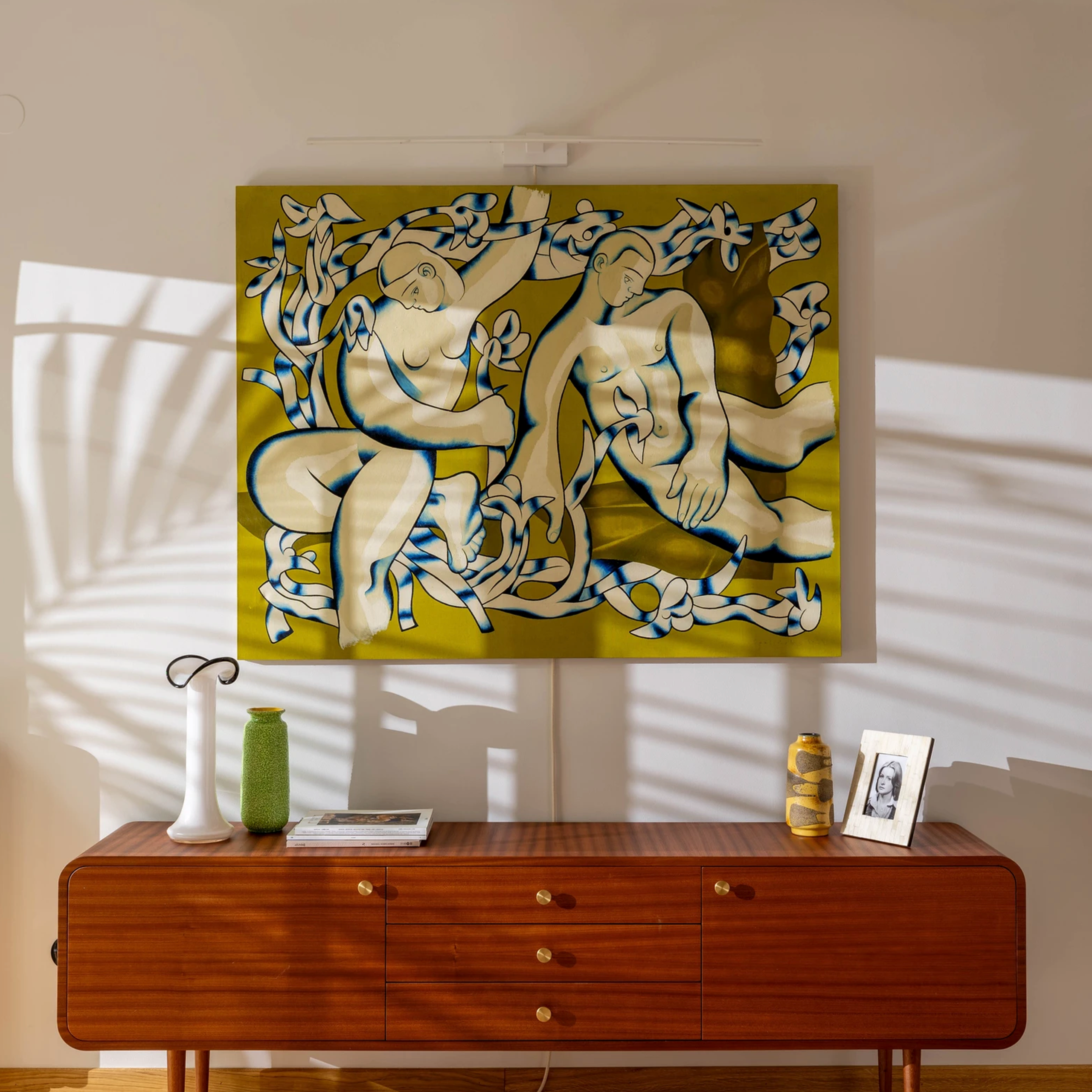 Nowoczesne wnętrze z designerskim fotelem, drewnianą komodą i kolorowym obrazem na ścianie.