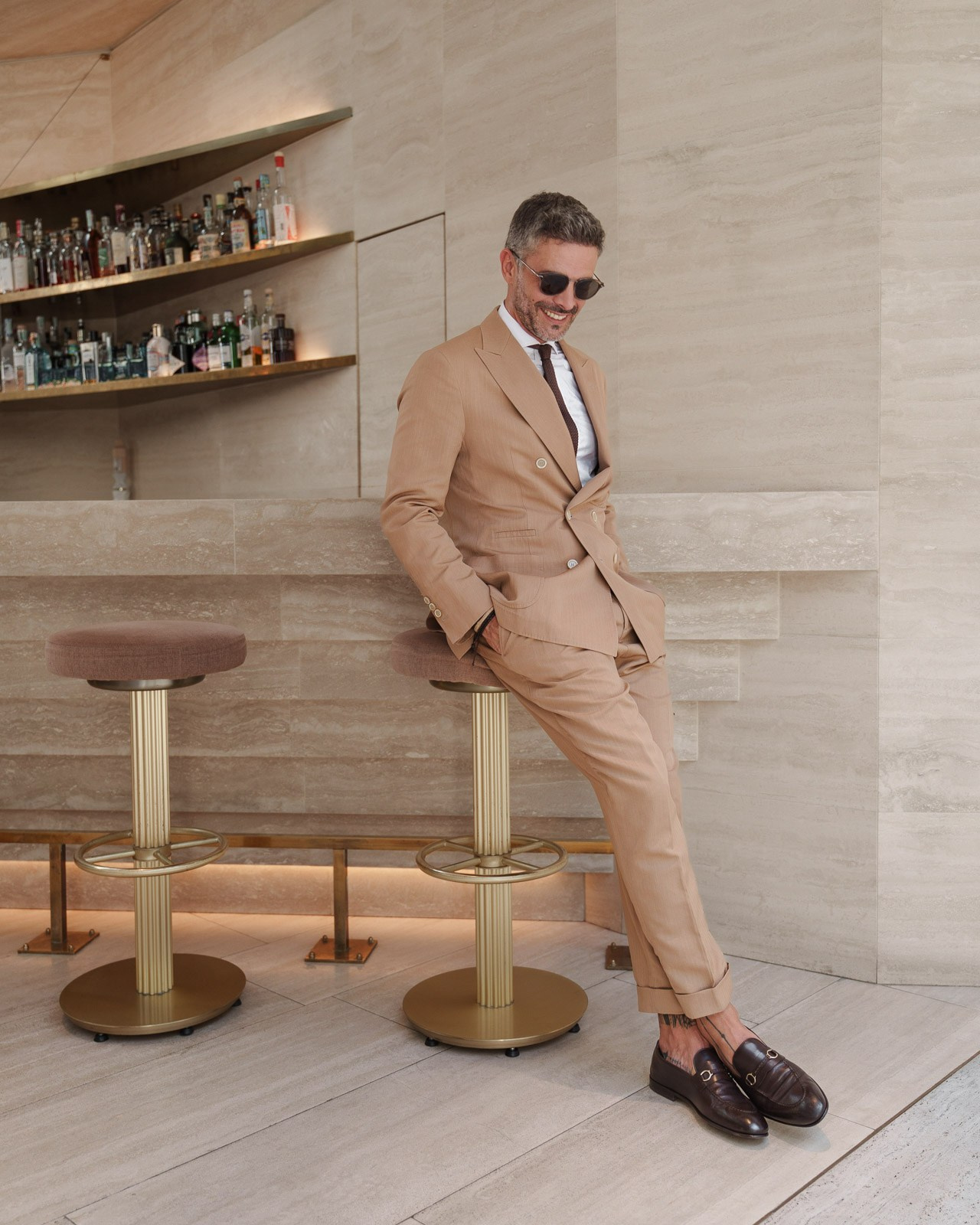 Male model in beige suit sitting at modern bar interior