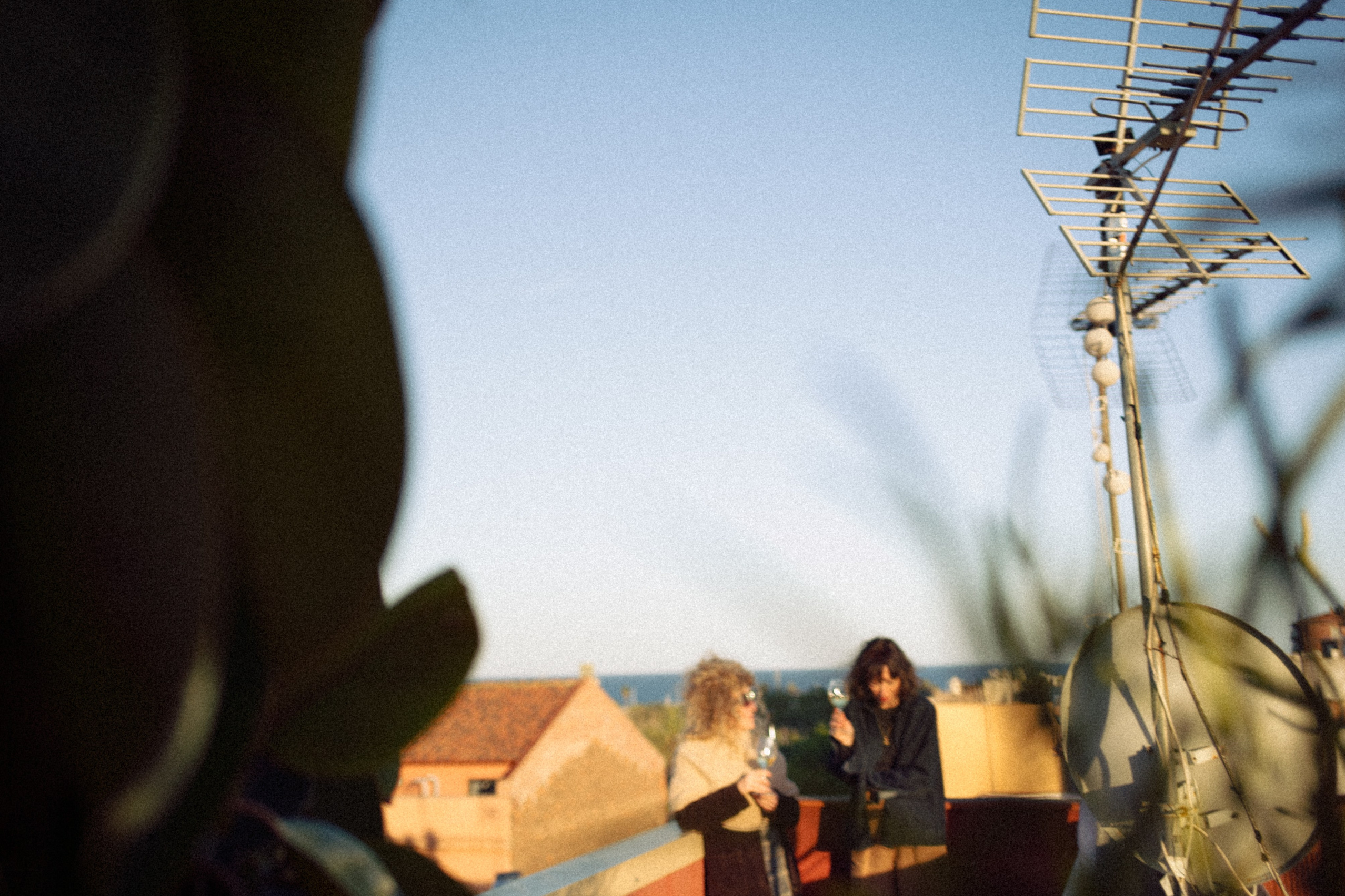 Blurred foreground silhouette of a person with a sharp focus on rooftops and two friends under a blue sky