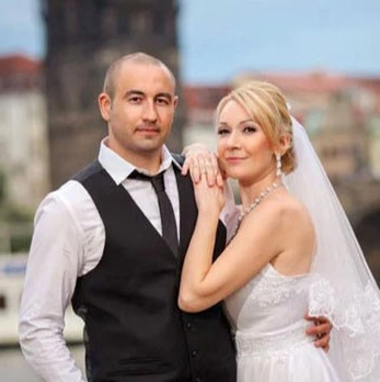 Smiling blonde-haired Swiss bride smiles lovingly towards her Italian groom as he looks towards the camera at a garden in Prague. 