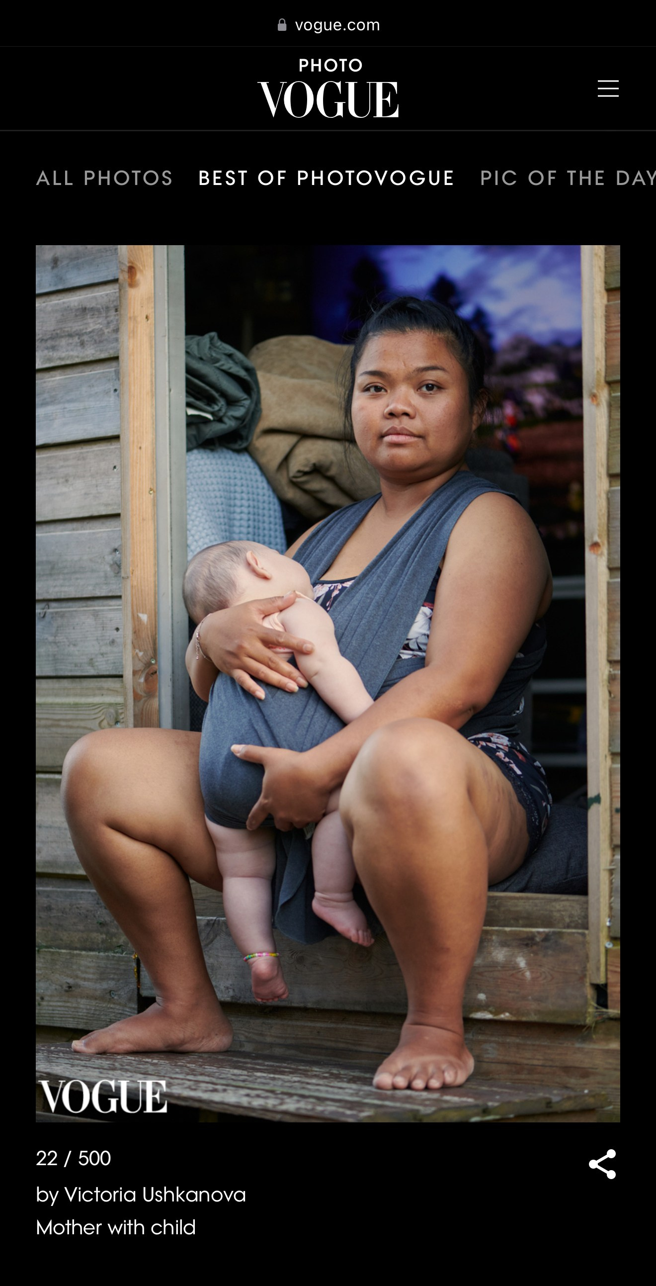 Een moeder zit in een houten deuropening en houdt haar slapende baby in een draagdoek. Ze kijkt in de verte met een kalme, vastberaden uitdrukking. Documentair portret door portretfotograaf Victoria Ushkanova.