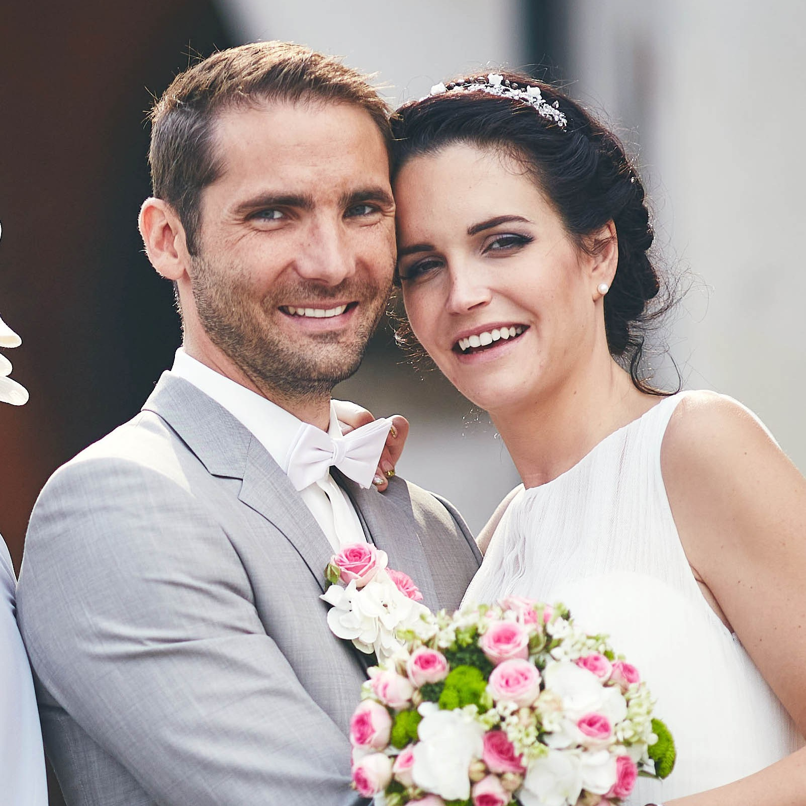 Red-haired bride holding her flowing veil aloft smiles seductively to her bouquet holding groom as he leans back against a railing in appreciation at the Vrtba Garden in Prague. 