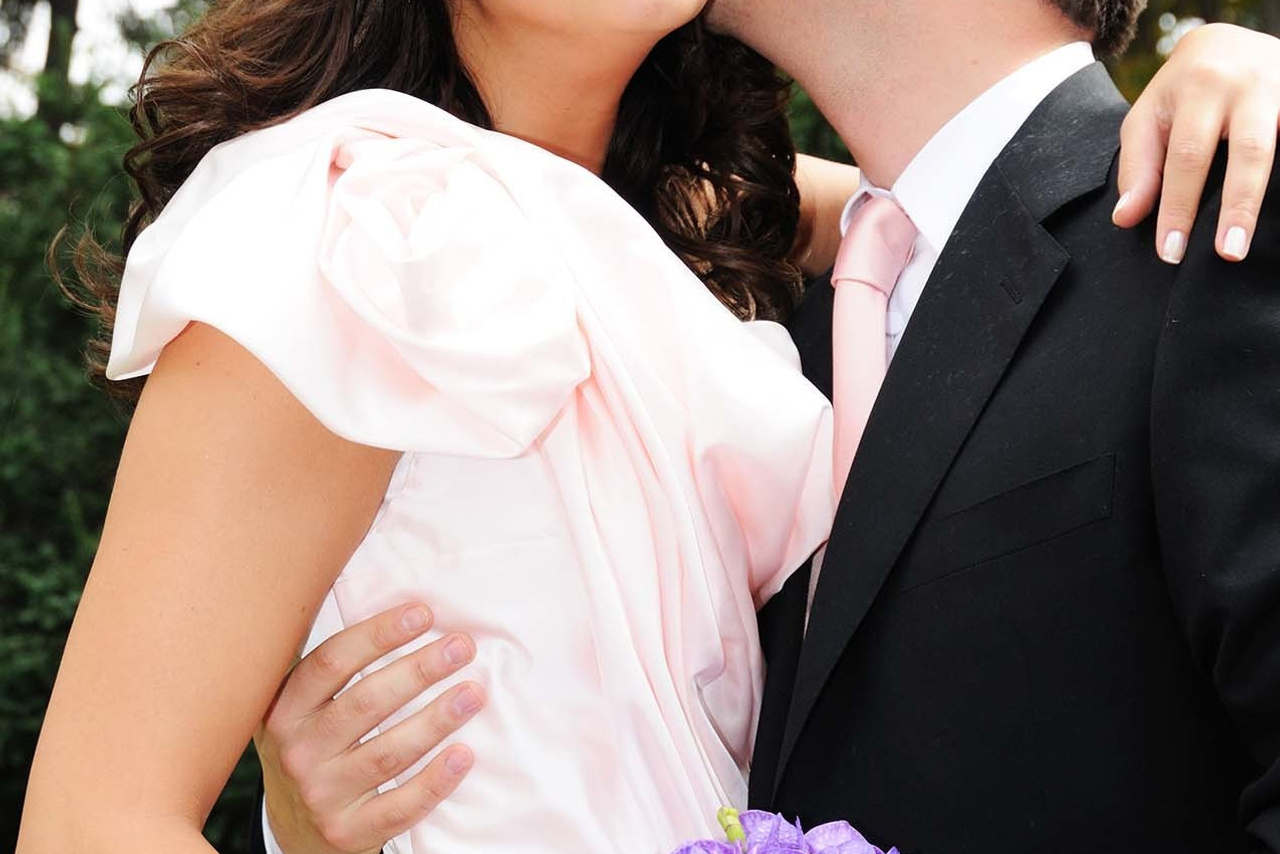 Groom kissing his smiling bride on the cheek as she holds a purple bouquet in an outdoor wedding setting