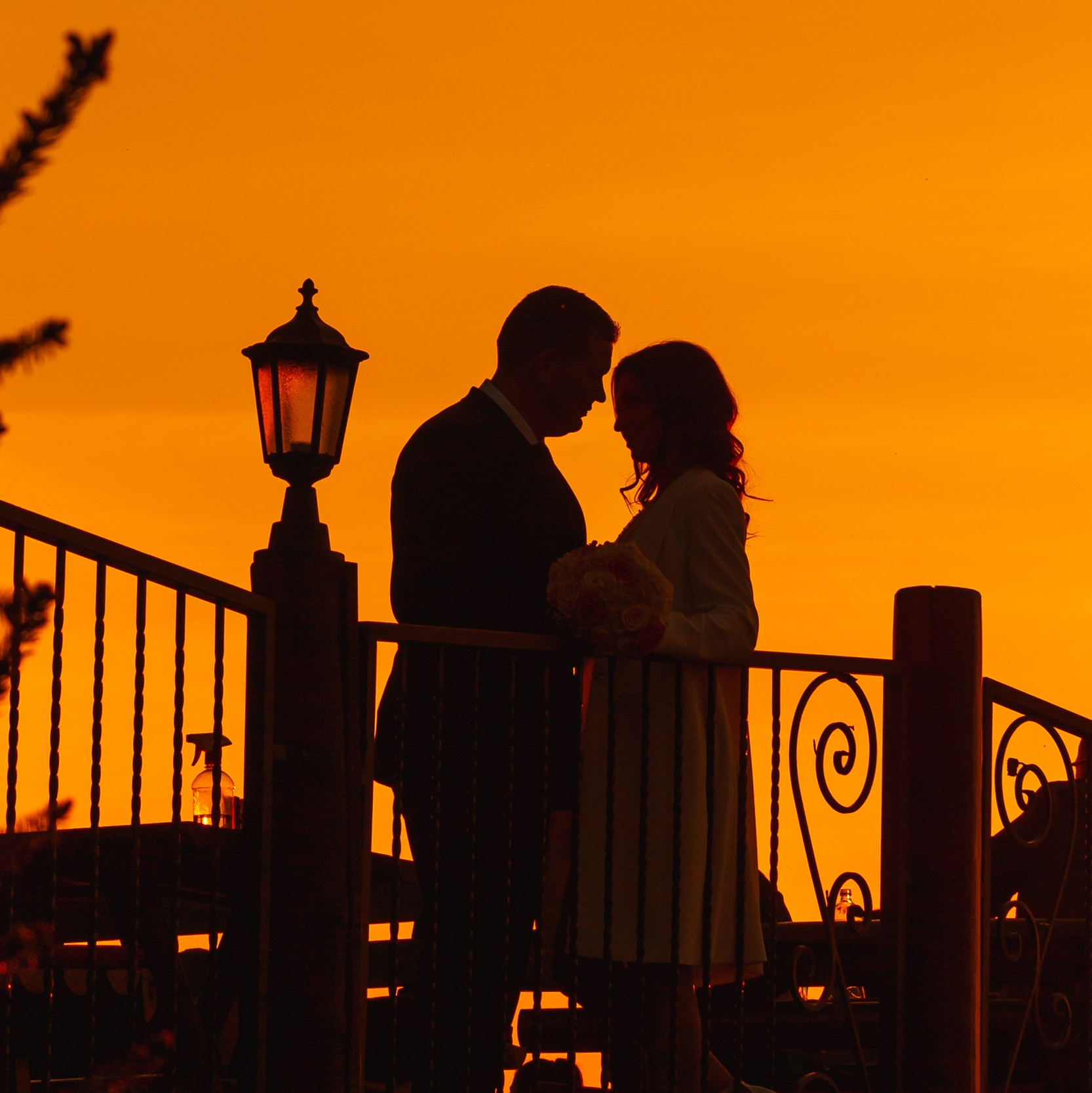 Silueta mladenaca u zagrljaju na zalasku sunca, obasjana toplim tonovima koji naglašavaju njihov poseban trenutak