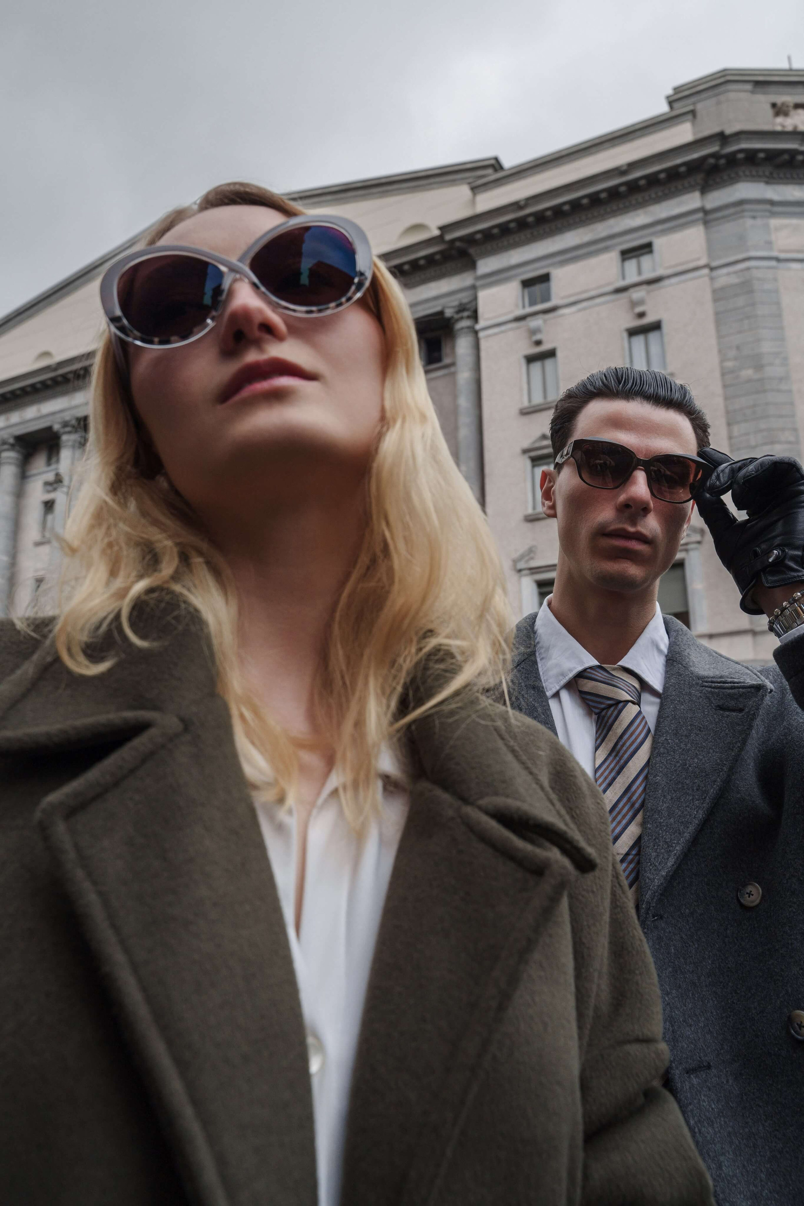Editorial-style fashion portrait of a couple wearing sunglasses, shot against a brutalist building in Milan