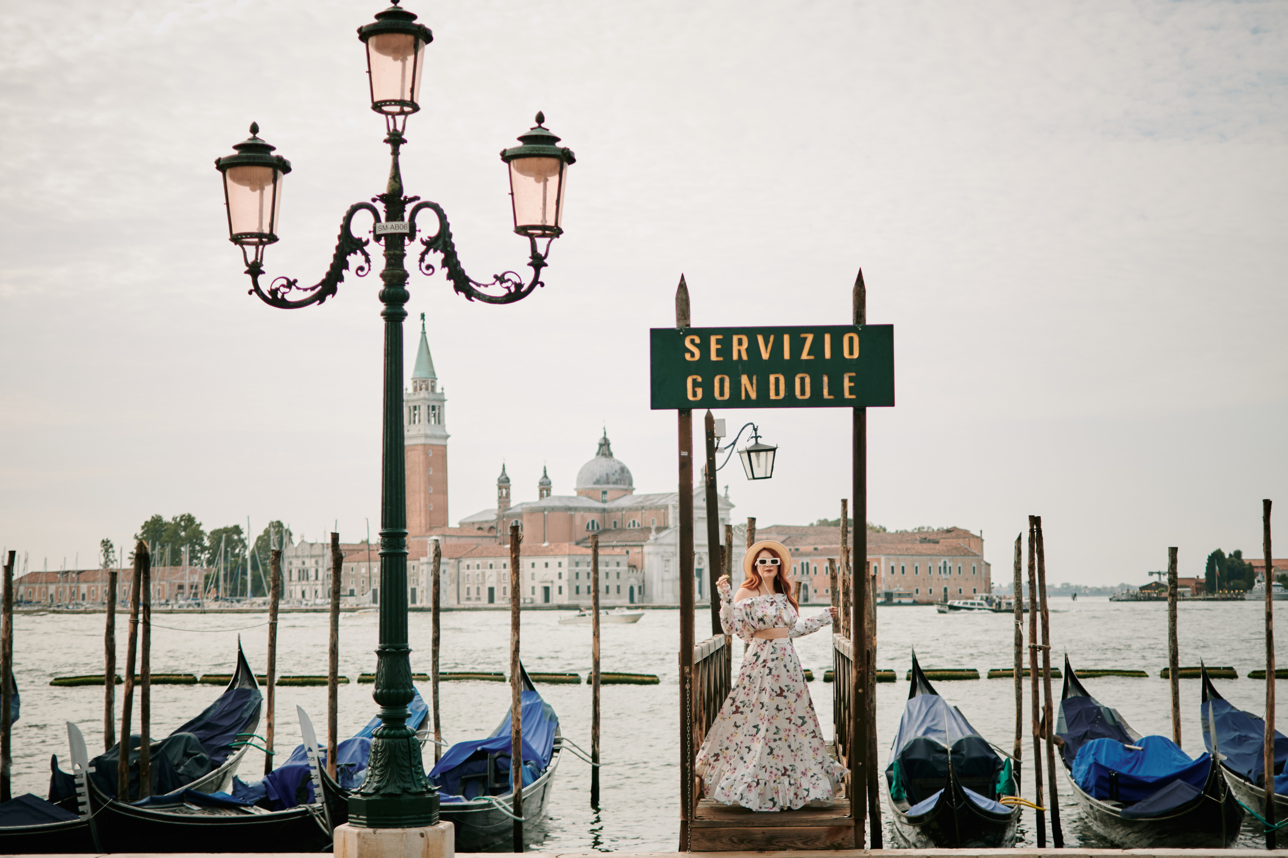 A young woman stands on San Marco Square, gazing at the stunning architecture and bustling crowds around her. The sun casts a warm glow on her face, highlighting her delicate features and soft, flowing hair. She wears a flowing dress that seems to dance in the breeze, accentuating her graceful movements. The intricate details of the nearby buildings and the vibrant colors of the street performers create a romantic and captivating atmosphere around her, making for a beautiful and memorable portrait. 