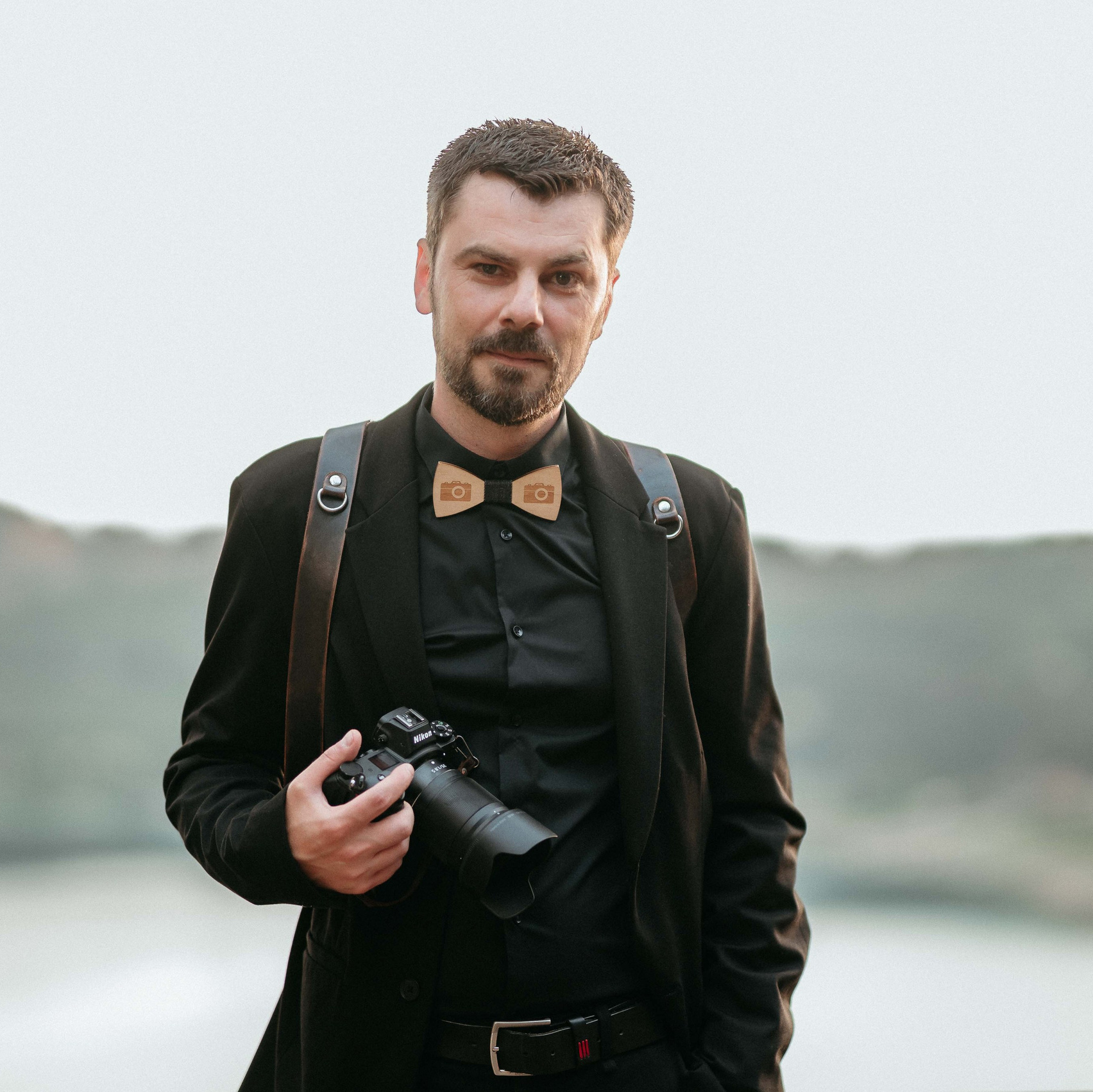 Ritratto di un fotografo di matrimonio con camicia bianca, esibendo con sicurezza una fotocamera professionale, il suo sguardo concentrato promette scatti memorabili e artistici.