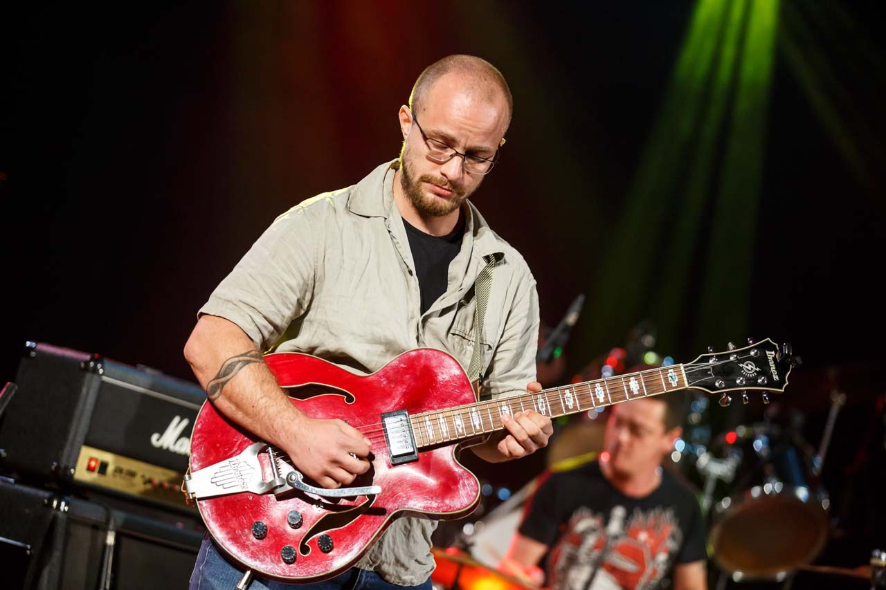 Energija na sceni sa fokusom na gitaristu tokom koncertnog performansa.