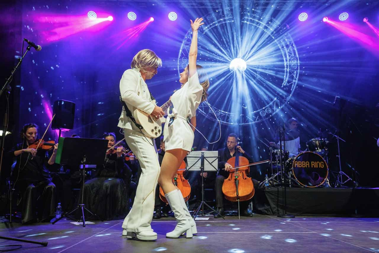 Emotivni trenutak pevačice i gitariste na sceni sa svetlosnim efektima u pozadini.