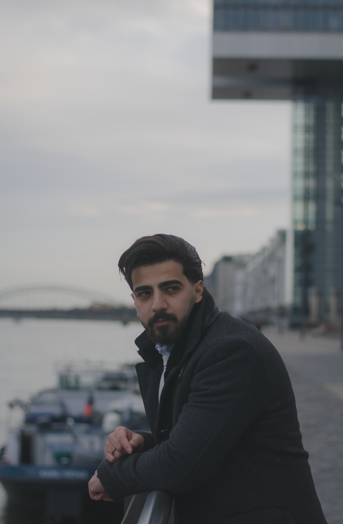 Porträt eines jungen Mannes mit schwarzen Haaren und Bart vor einem Flussufer Hintergrund