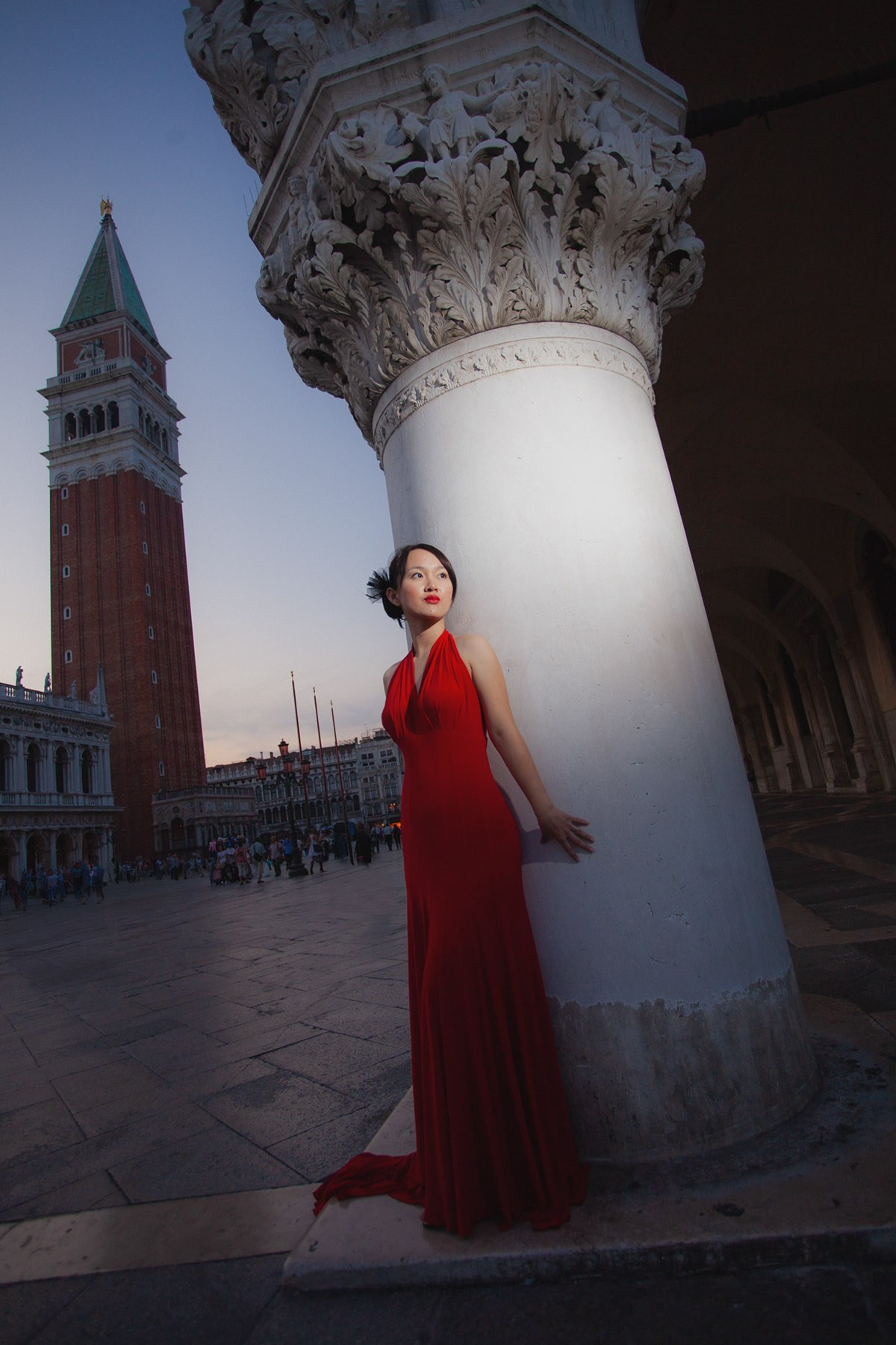 A Thai woman in the red dress poses against a historic column at the Doge's Palace in Venice during her pre-wedding portrait session.