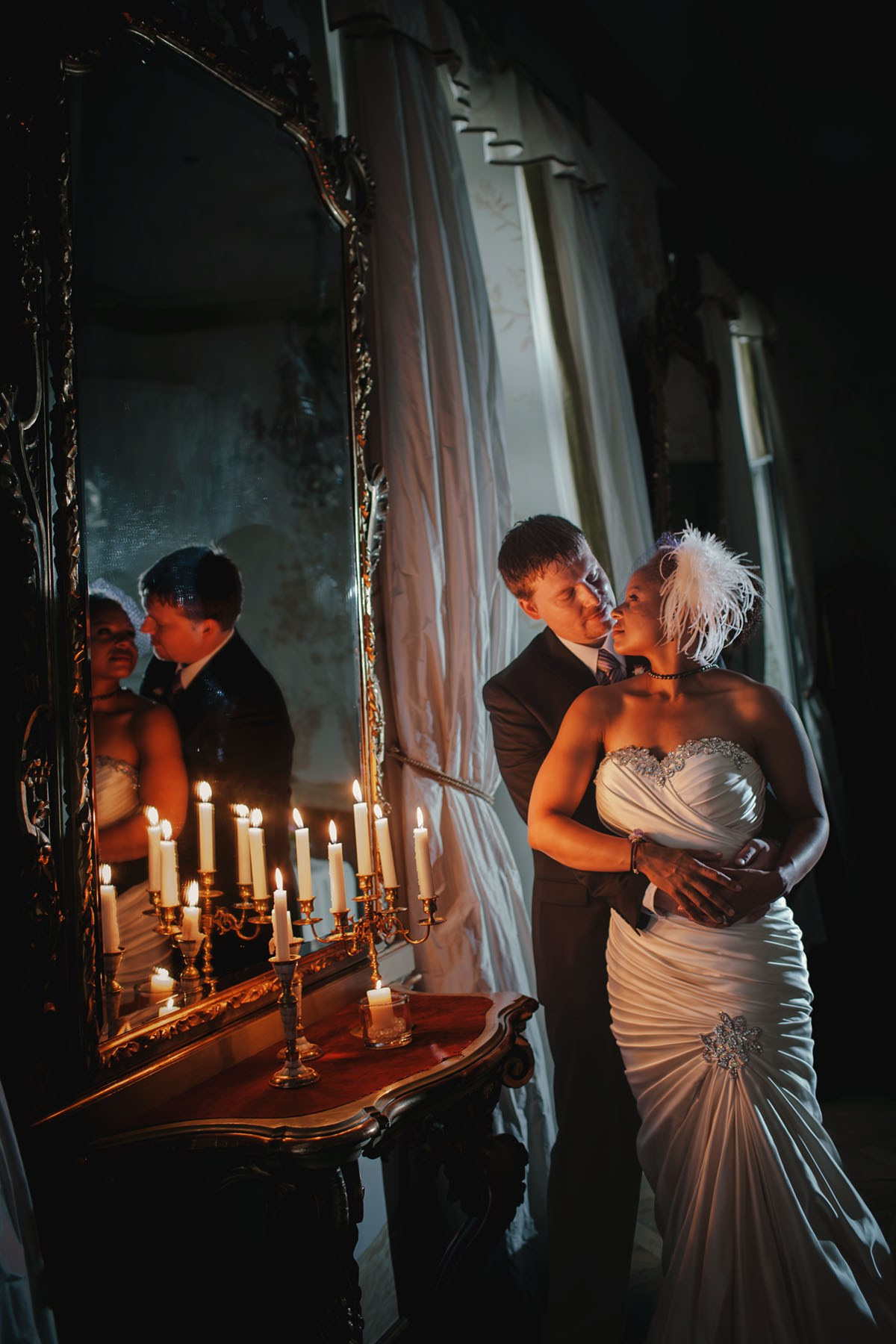 American bride and groom sharing an embrace next to a historic mirror in the candlelit ambiance of Chateau Mcely."