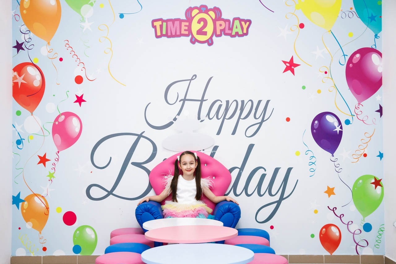 Slavljenica ispred šarene rođendanske pozadine sa balonima i natpisom ‘Happy Birthday’