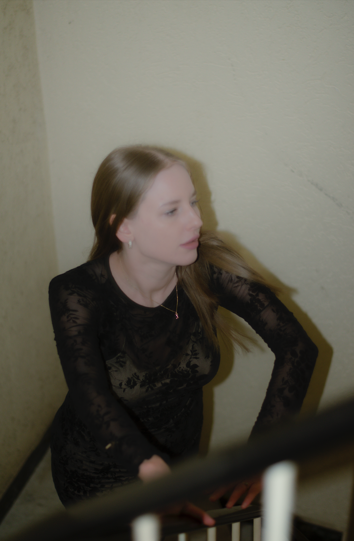 Porträt einer jungen Frau mit dunkelblonden Haaren und schwarzem Spitzenkleid stehend im Treppenhaus