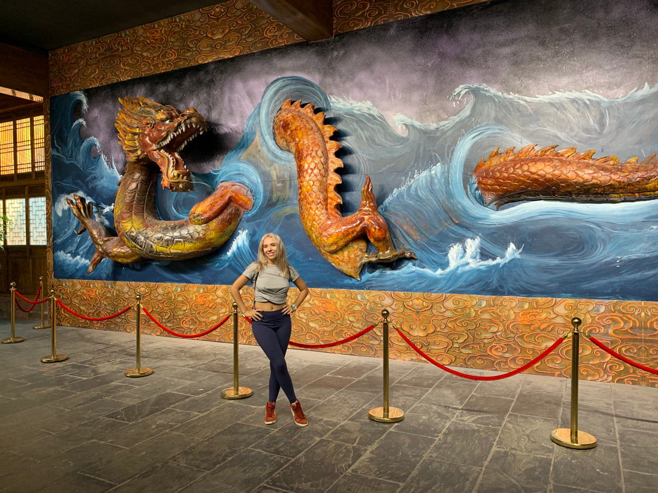 a girl standing in front of a wall with a dragon sculpture