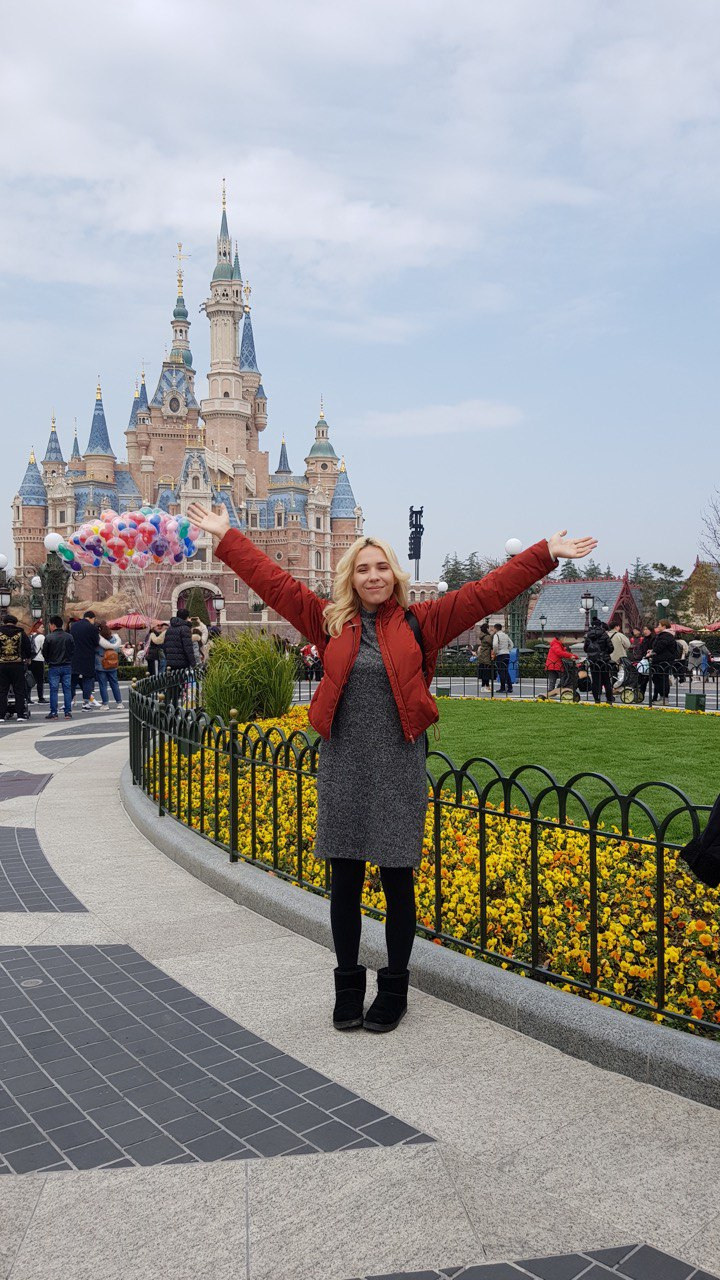 blond woman in a red jacket in Shanghai Disneyland with a castle in the background