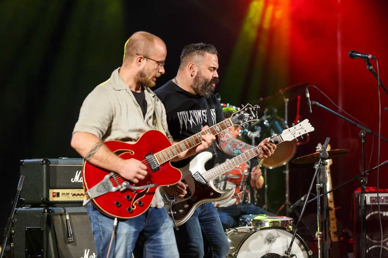 Dvojica gitarista Moonshine Alligators benda u intenzivnom zajedničkom performansu na koncertnoj pozornici.