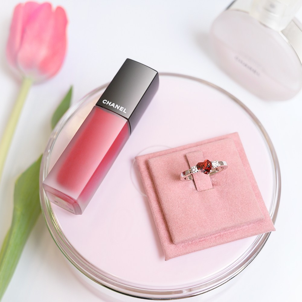 Zlatni prsten sa rubinom stoji na stolu pored karmina i lale.