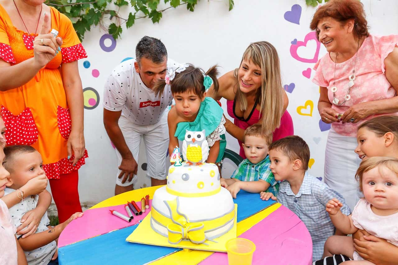 Vesela porodica duva svećice, okupljena na šarenom rođendanskom slavlju.